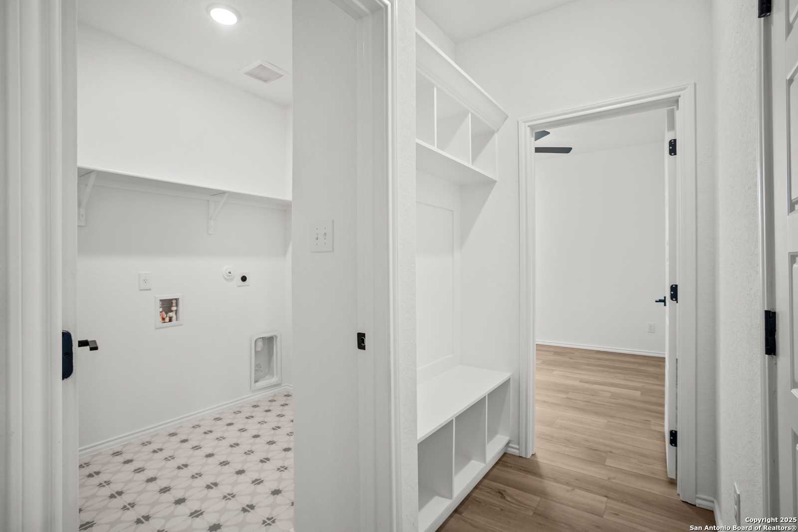 Bright laundry room with washer/dryer hookups, patterned tile floor, and adjacent closet shelving in Davidson Homes The Daphne K, San Antonio