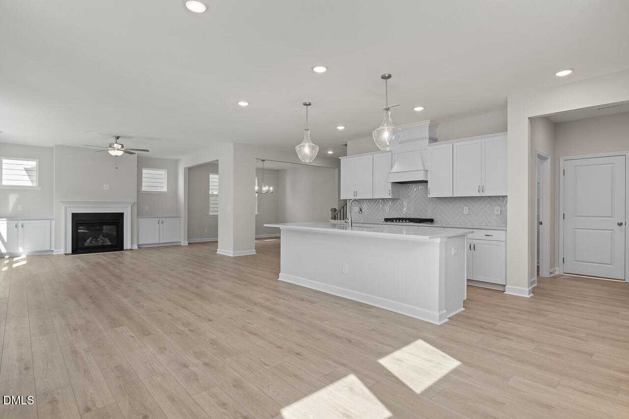 Open-concept kitchen and living area with white island, gas range, stone fireplace, and light hardwood floors in Davidson Homes The Beech C, Wake Forest, NC