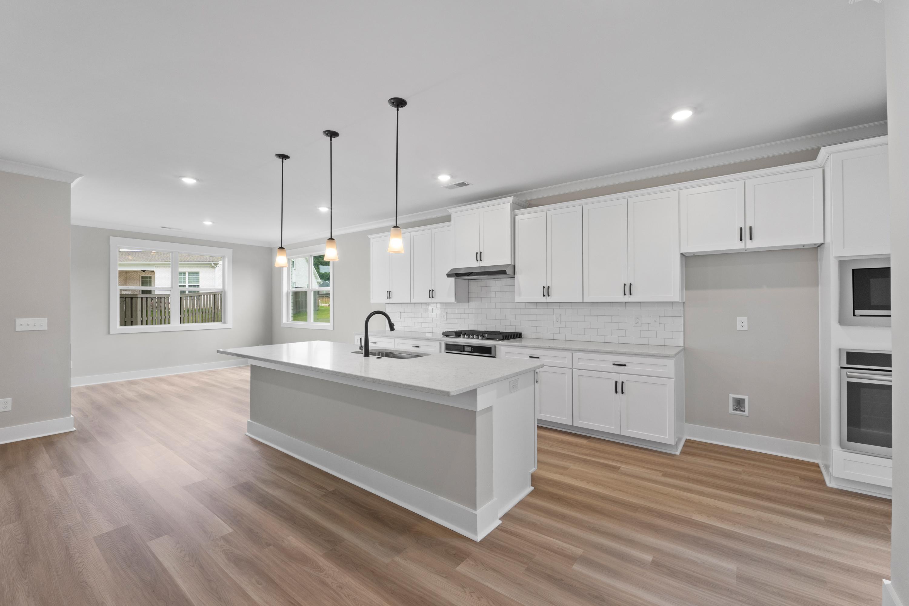 Spacious white kitchen in The Oxford home design featuring large island, stainless appliances, subway tile backsplash