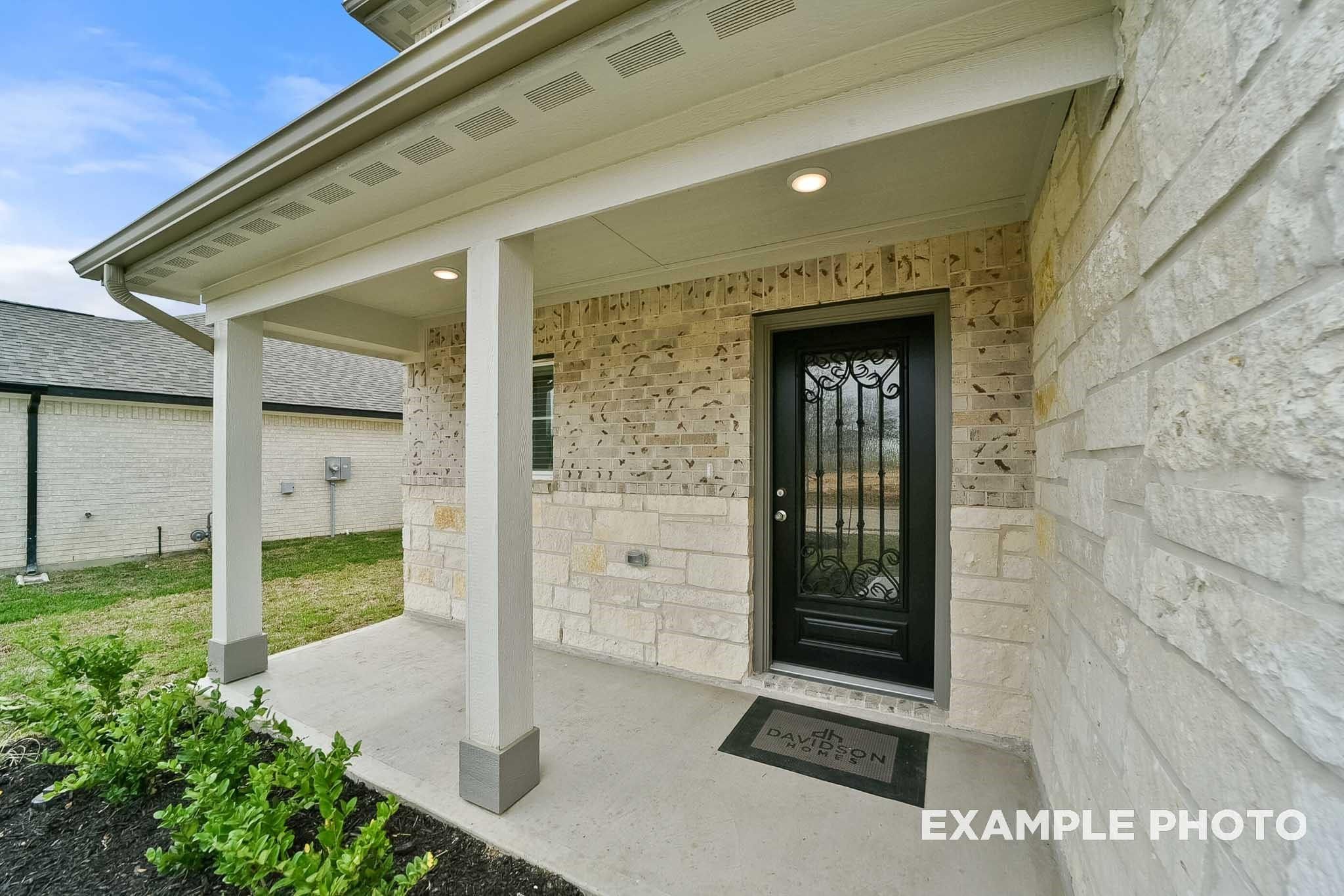 Elegant wrought-iron front door with covered porch and stone facade on Davidson Homes The Tierra B in Emberly, Beasley, Texas