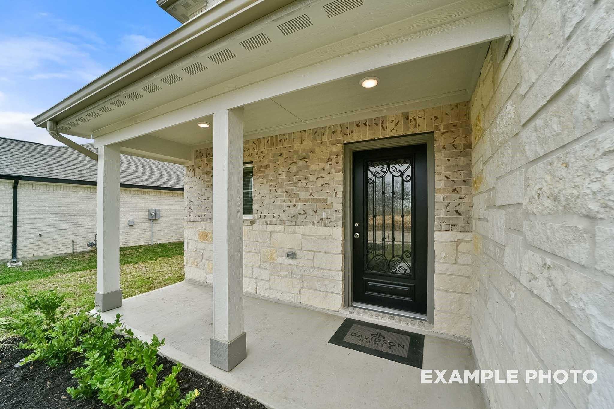 Elegant wrought-iron front door with covered porch and stone facade on Davidson Homes The Tierra B in Emberly, Beasley, Texas