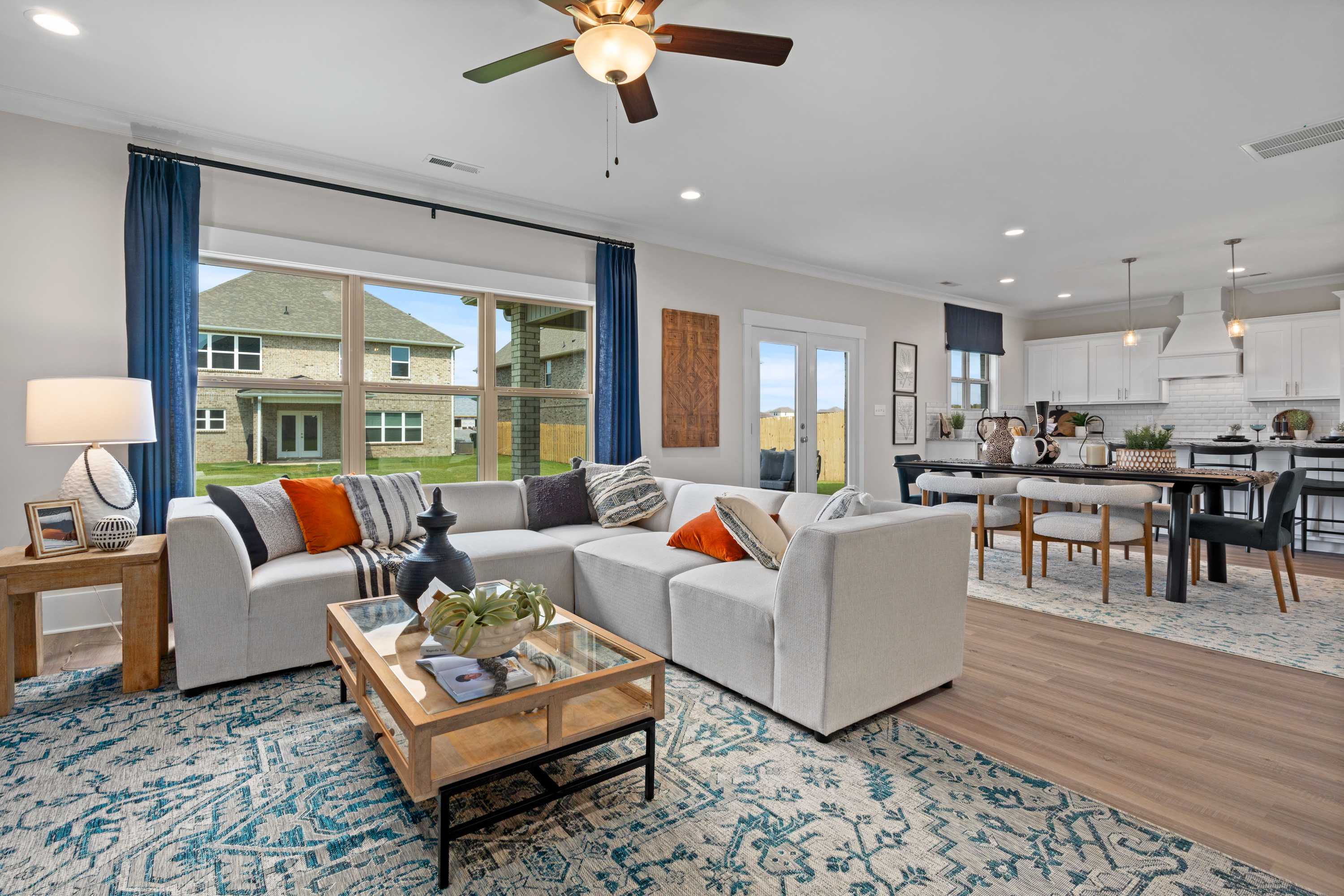 Open-concept living room in The Chelsea B showcasing white L-shaped sofa, wooden coffee table, blue rug, and dining nook view