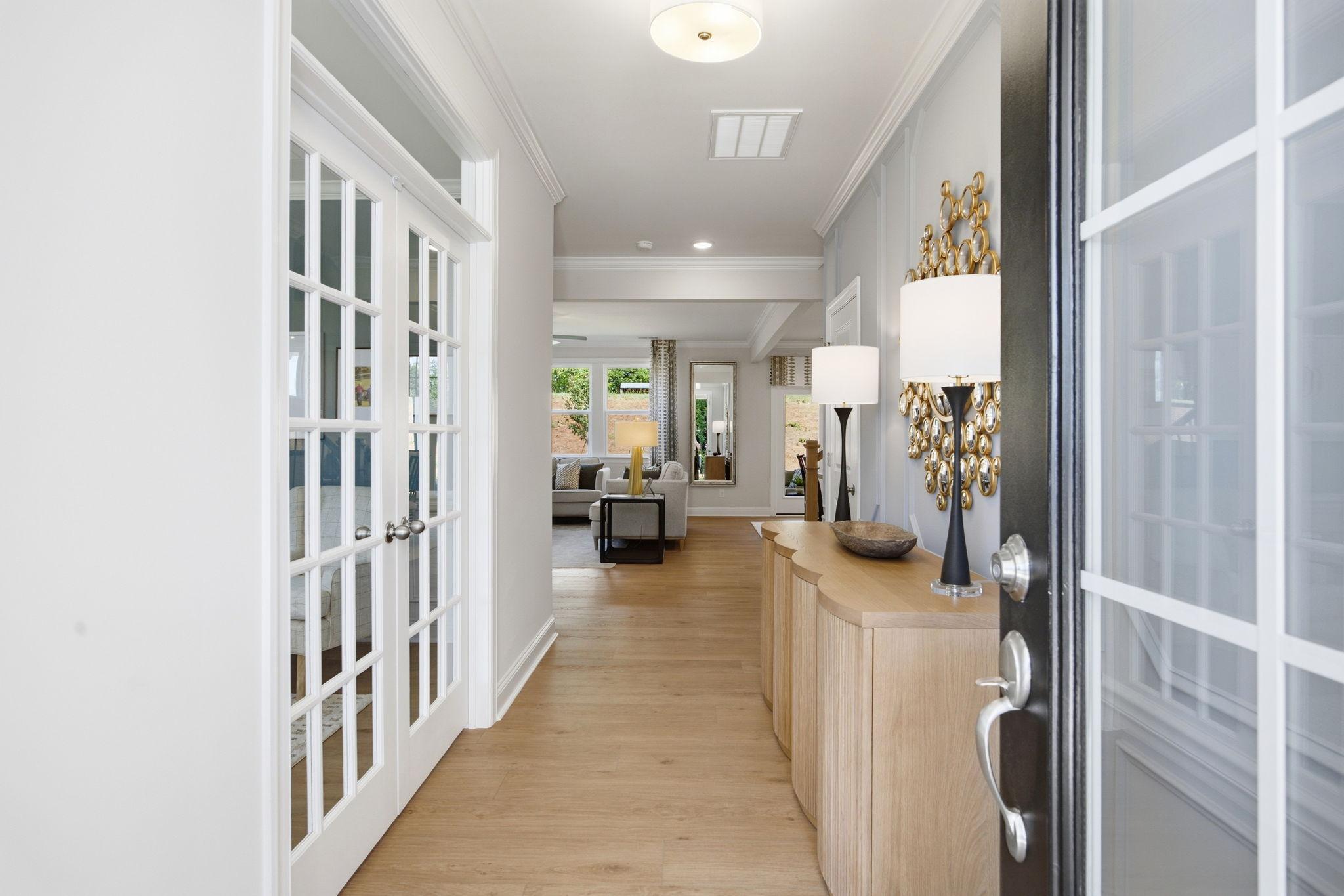 Spacious entry hallway with oak hardwood floors, white French doors, and console table at Enclave at Belmont in Belmont NC