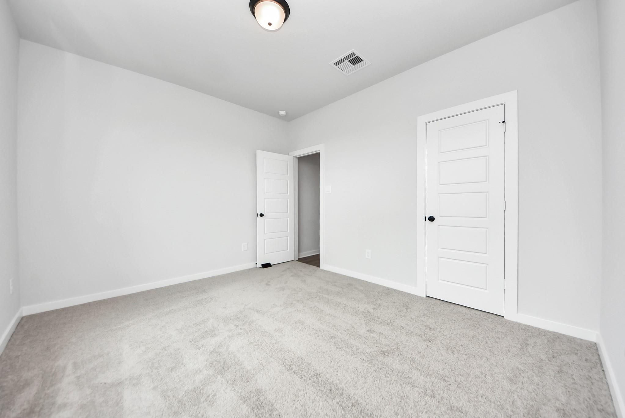 Spacious secondary bedroom with plush carpet and modern doors in The Daphne F floor plan at Sundance Cove, Crosby, Texas.