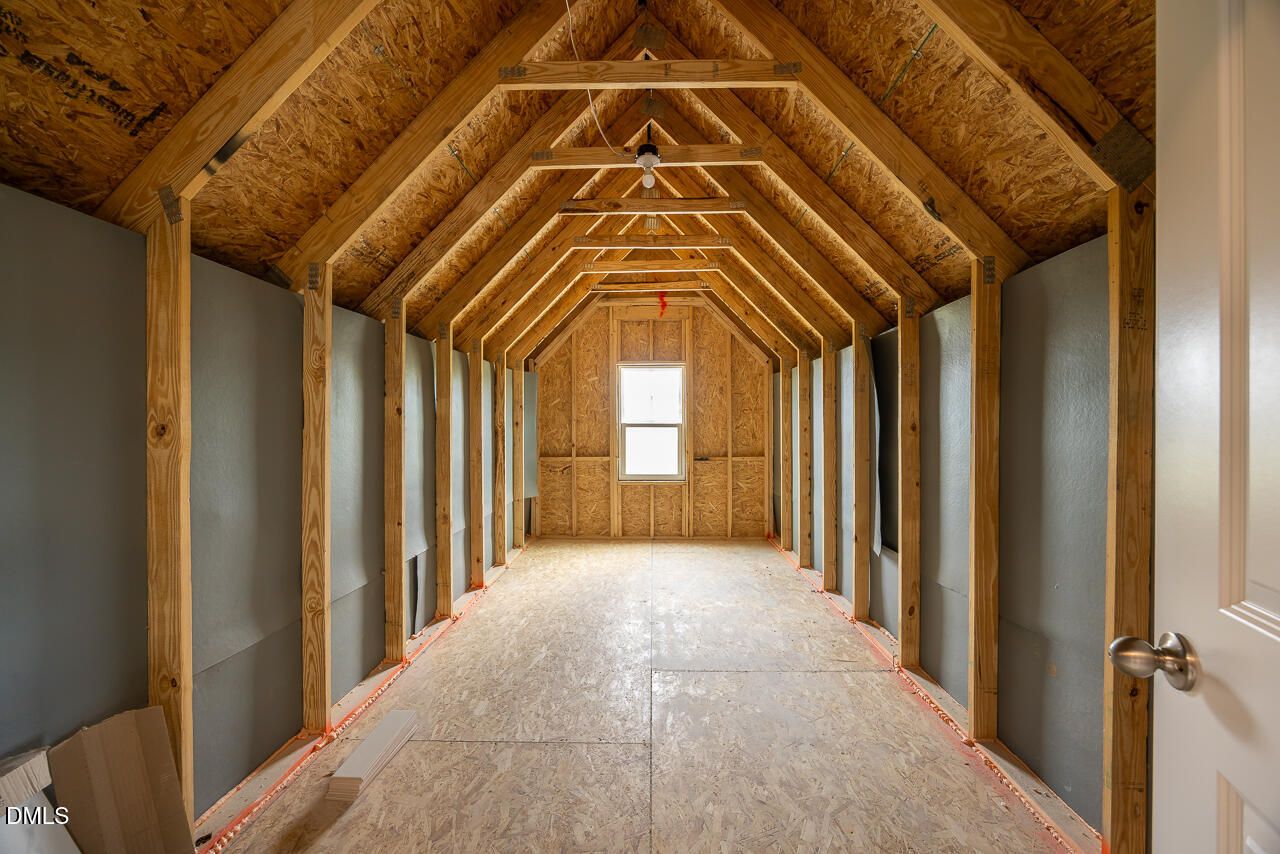 Unfinished bonus room with exposed wooden rafters, plywood walls and floor, small window in Davidson Homes The Ash B, Lillington, NC