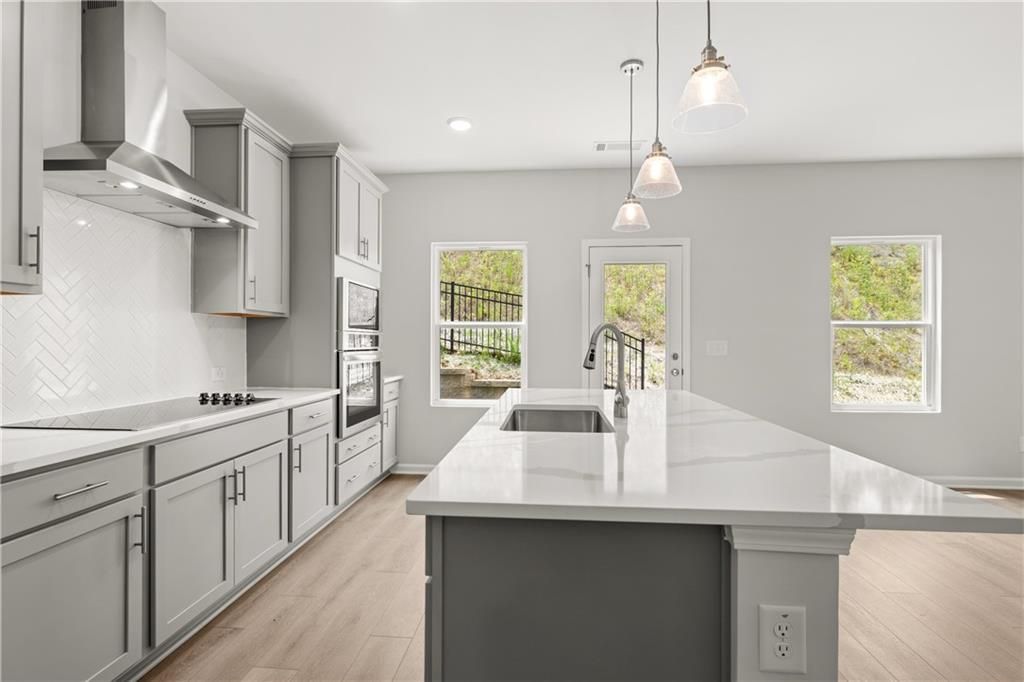 Modern kitchen with large quartz island, grey cabinetry, and herringbone backsplash in The Burton A home, Canton, Georgia.