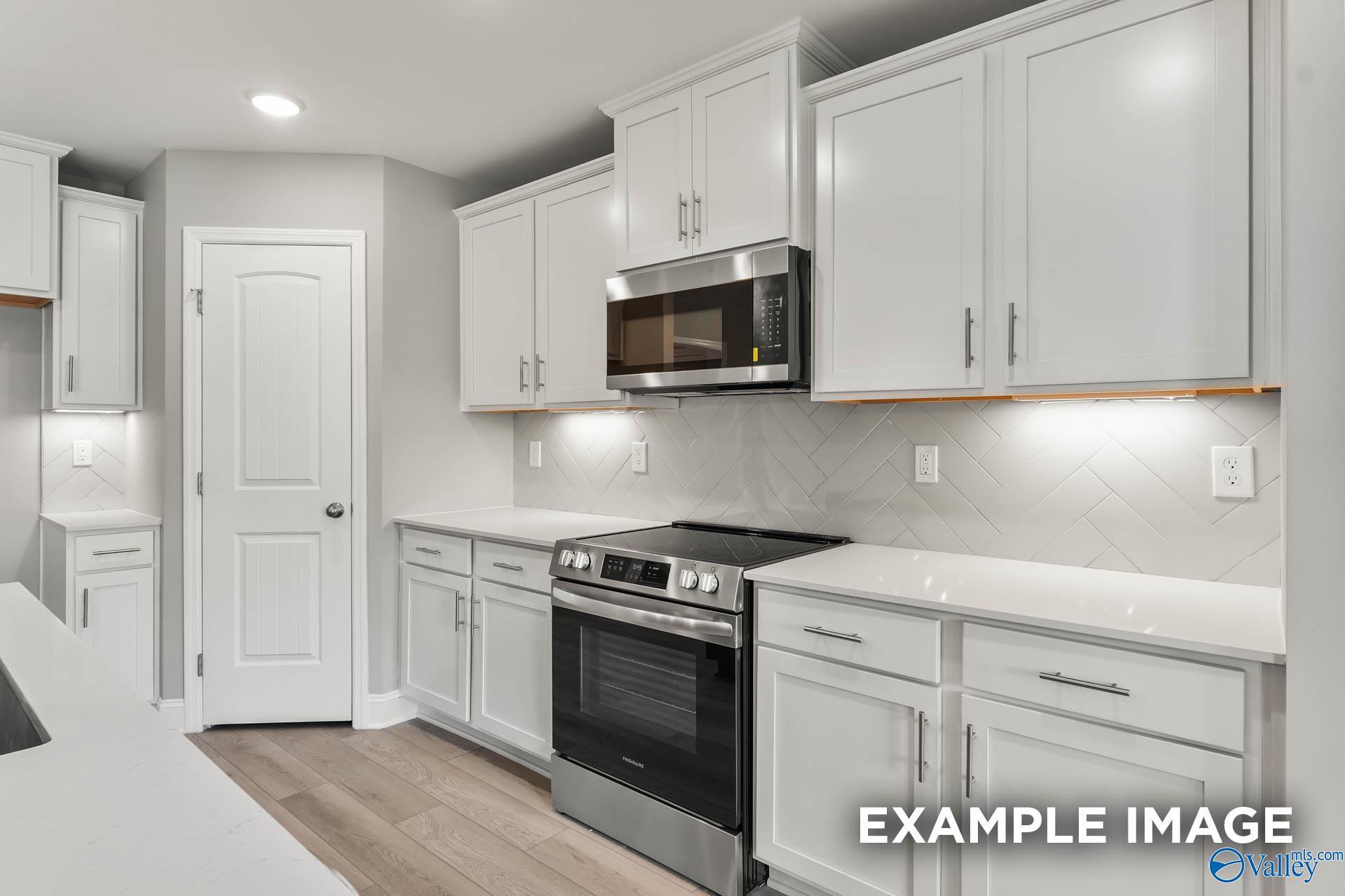 Modern white kitchen with quartz counters, stainless steel range, herringbone backsplash in The Everett B, Toney, AL