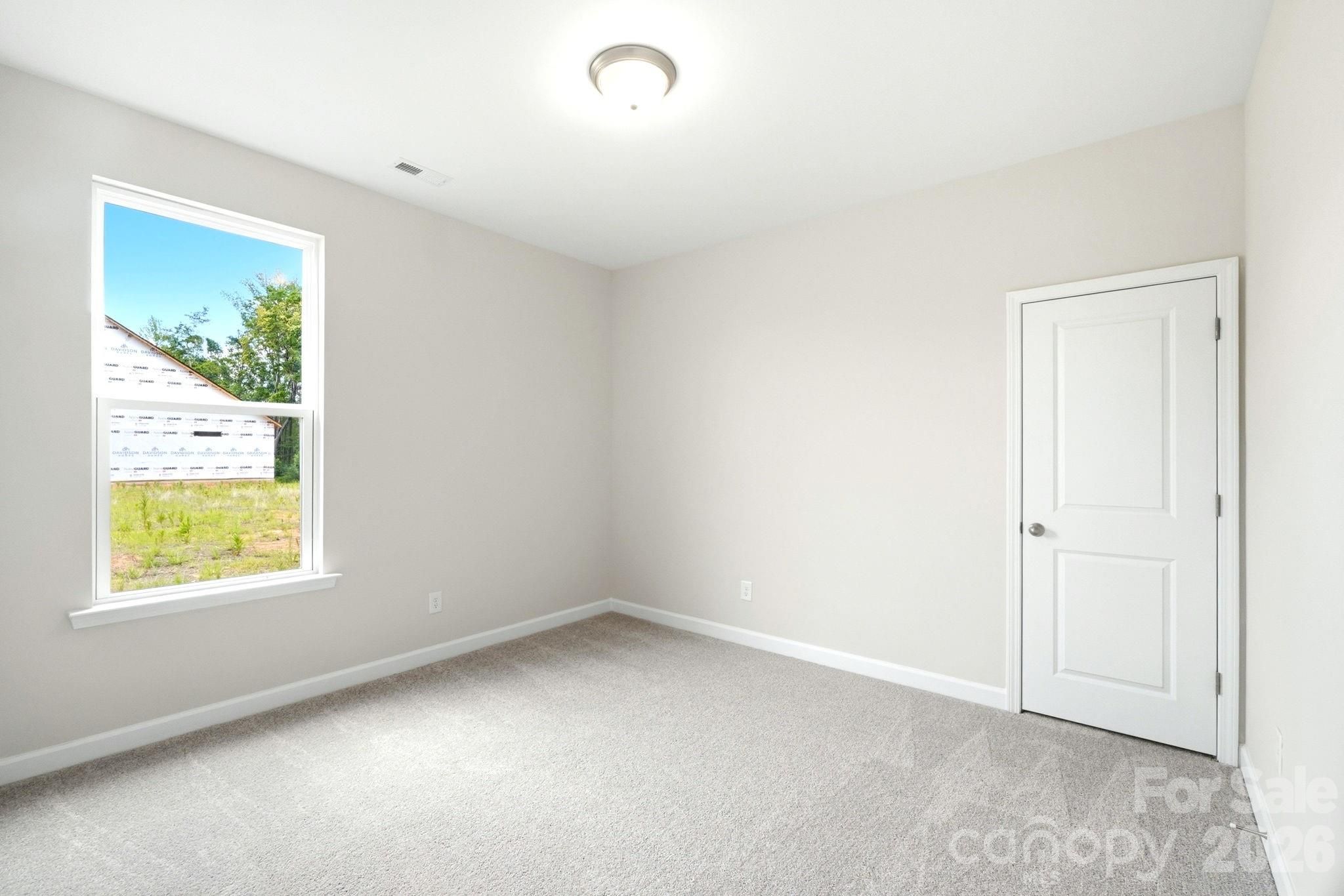 Bright neutral bedroom with carpet and white door in The Magnolia B floor plan by Davidson Homes in Windgate, Mooresville.