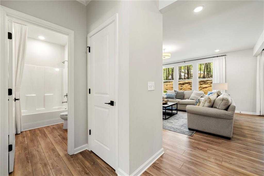 Modern bathroom with white tub and shower opening to cozy living room with beige sofa in Davidson Homes The Hickory B, Riverwood, Dallas, GA