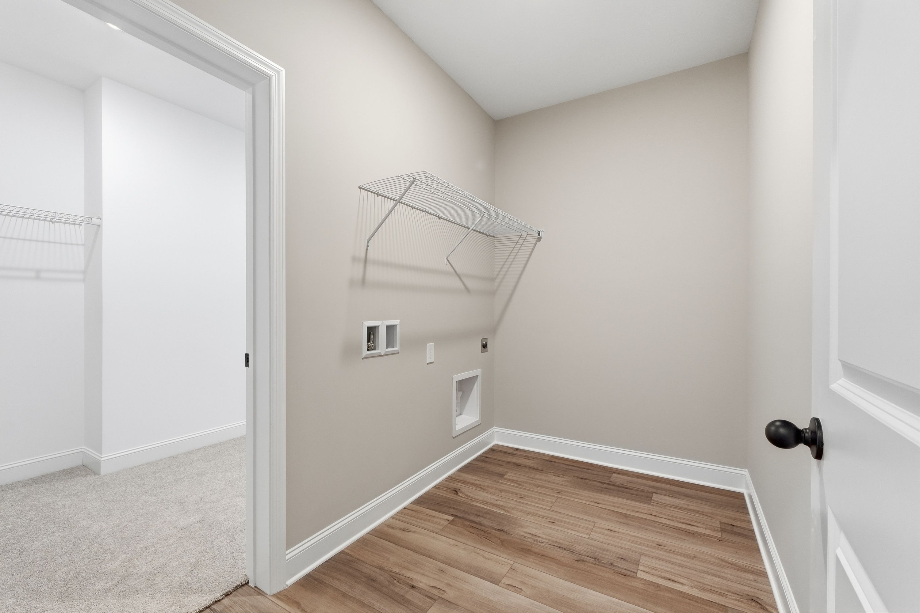 Spacious laundry room in The Rockford Davidson Homes design featuring beige walls, hanging rod, washer dryer hookups, and wood flooring