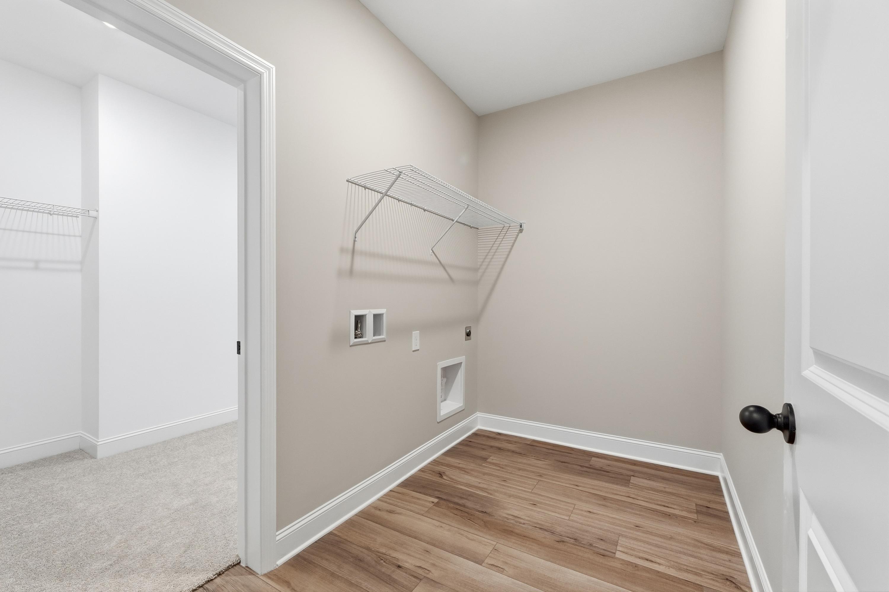 Spacious laundry room in The Rockford Davidson Homes design featuring beige walls, hanging rod, washer dryer hookups, and wood flooring