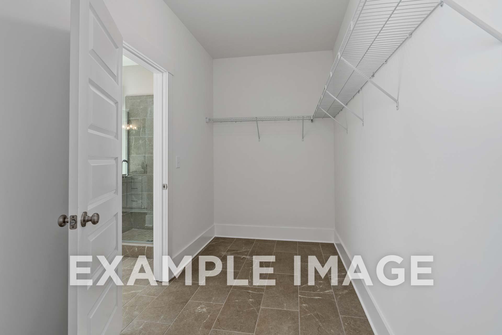 Spacious walk-in closet in The Harrison B master suite with wire shelving, white walls, and adjacent bathroom door