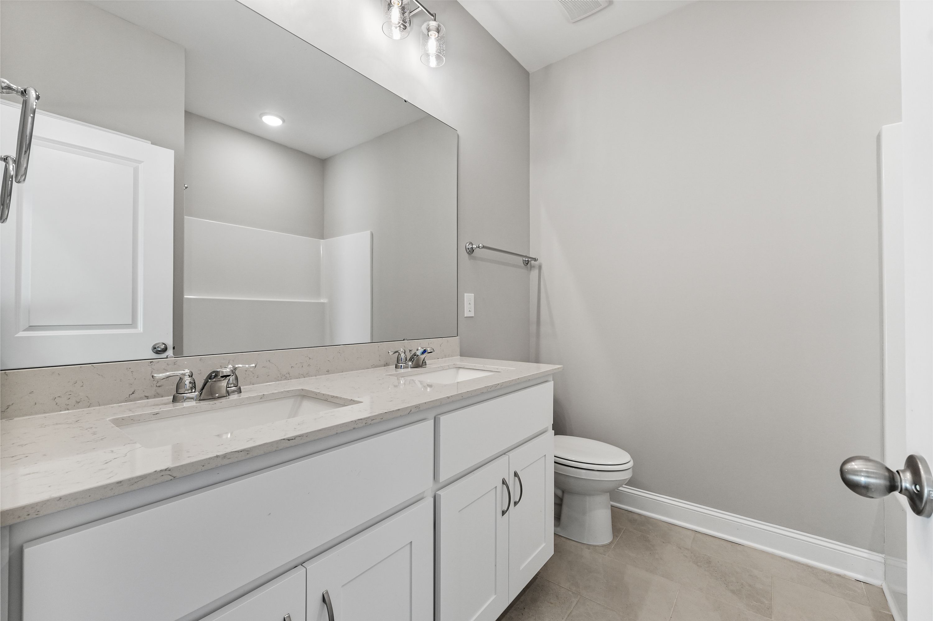Spacious master bathroom in The Valencia featuring double vanity sinks, large frameless mirror, walk-in shower, and modern gray tones
