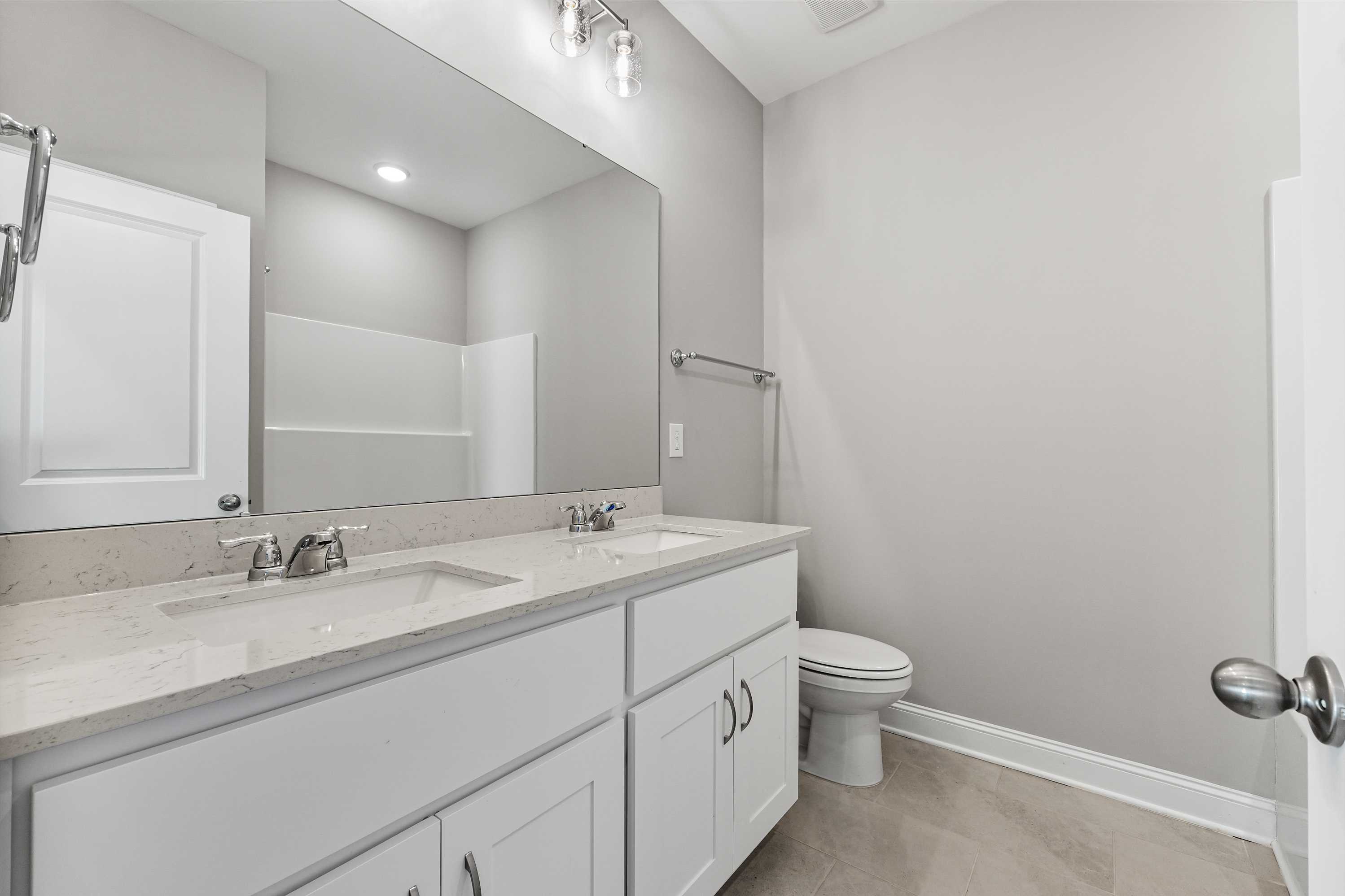 Spacious master bathroom in The Valencia featuring double vanity sinks, large frameless mirror, walk-in shower, and modern gray tones