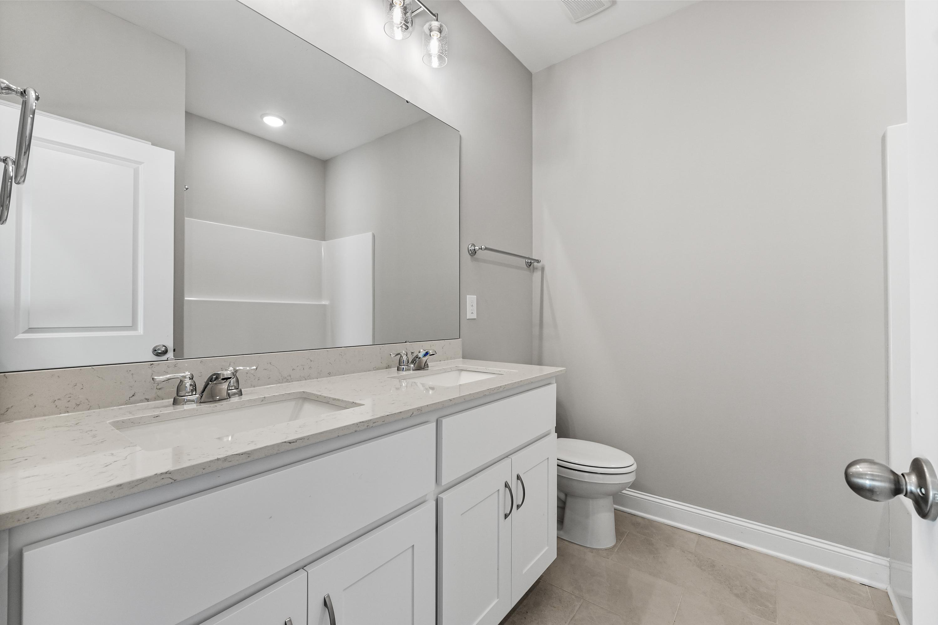 Spacious master bathroom in The Valencia featuring double vanity sinks, large frameless mirror, walk-in shower, and modern gray tones