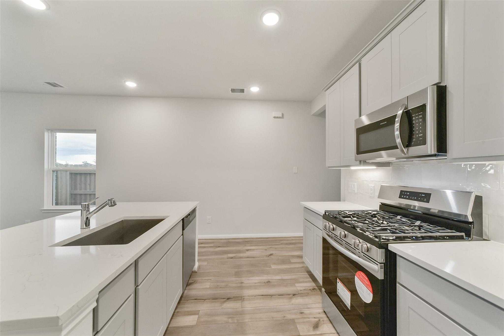 Modern white kitchen with stainless appliances, quartz island sink, and hardwood floors in Davidson Homes San Marcos E, Beasley TX