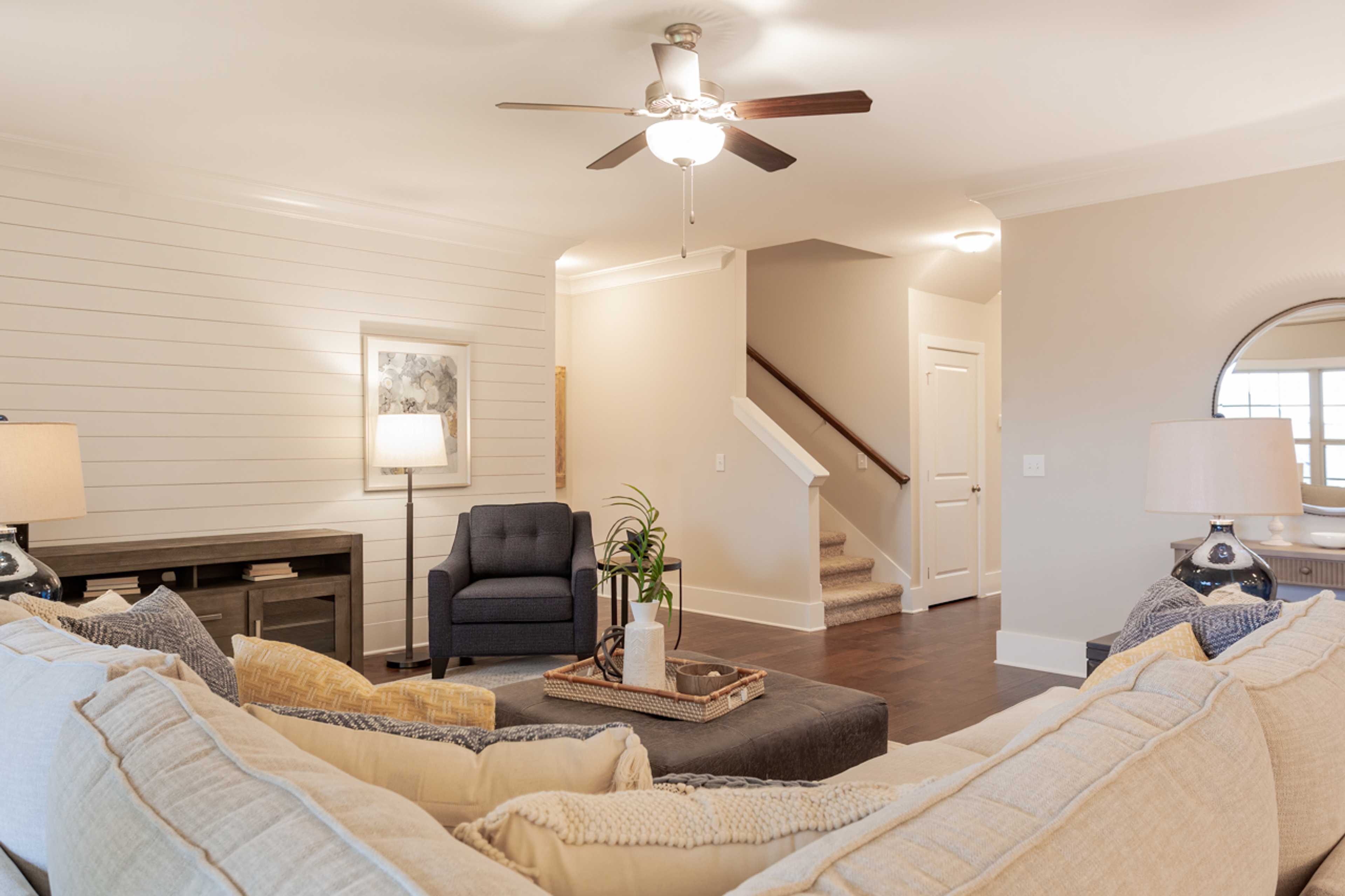 Open-concept living room in Laurenwood Preserve, Madison AL with shiplap walls, hardwood floors, ceiling fan, and modern gray sectional sofa