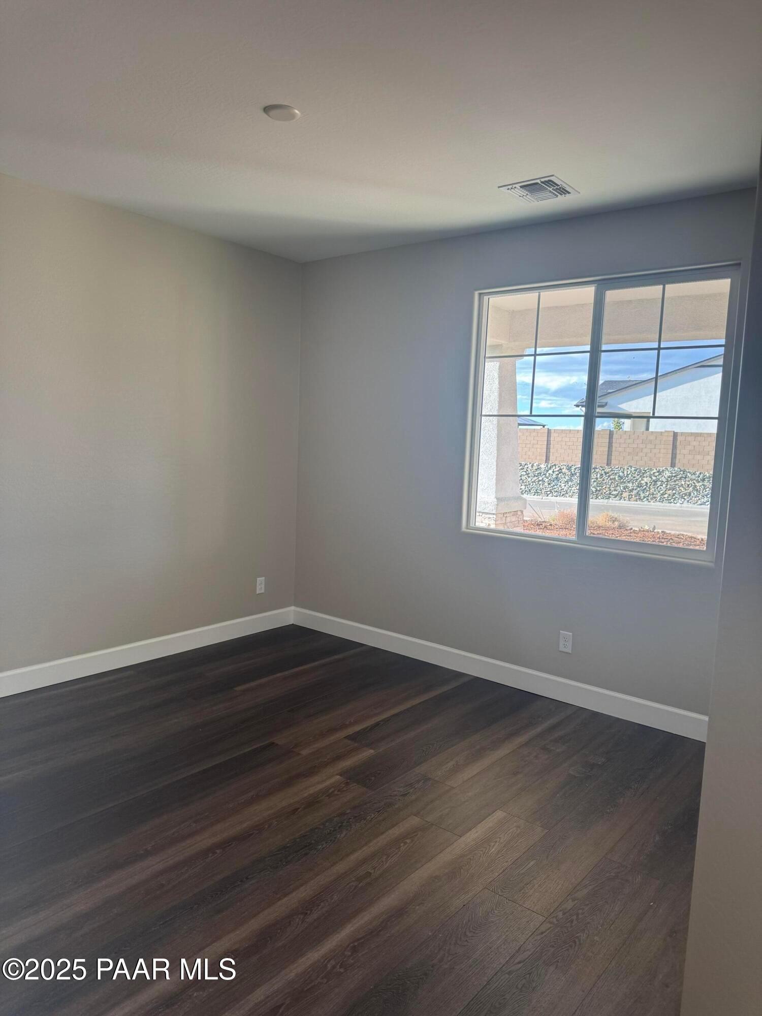 Bright bedroom with beige walls, large sliding window overlooking desert mountains, and hardwood floors in Evermore Homes The Sunrise A, Prescott Valley