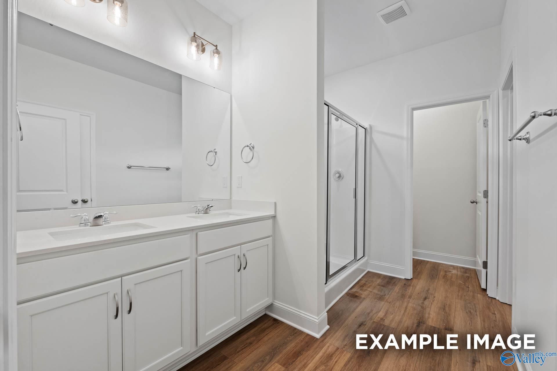 Modern master bathroom featuring double white vanity, walk-in glass shower, and hardwood floors in Evermore Homes Daphne E, Harvest, AL