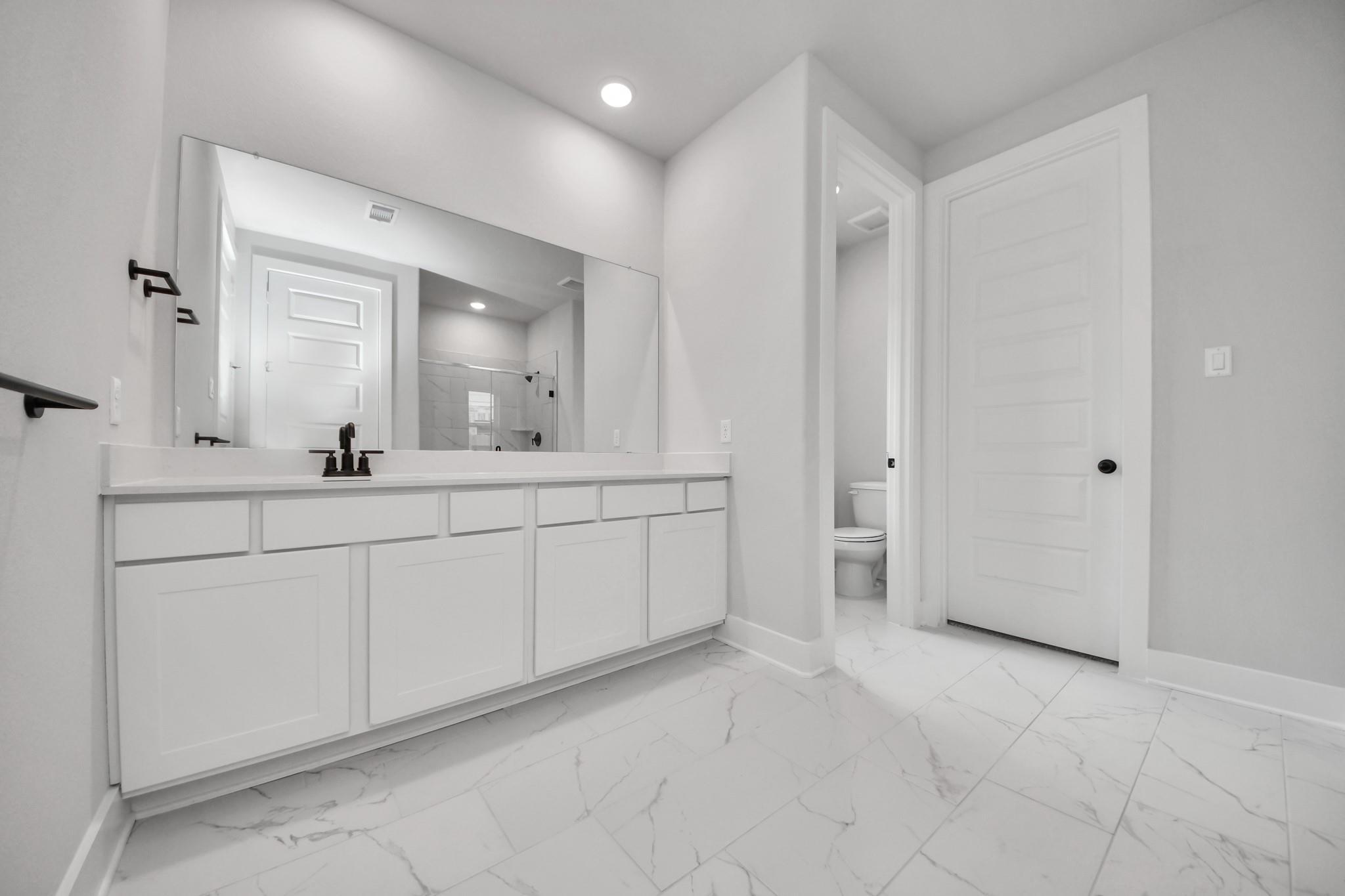 Modern bathroom with white vanity, marble-look tile flooring, and mirror in a Davidson Homes Laguna C floor plan in Katy.