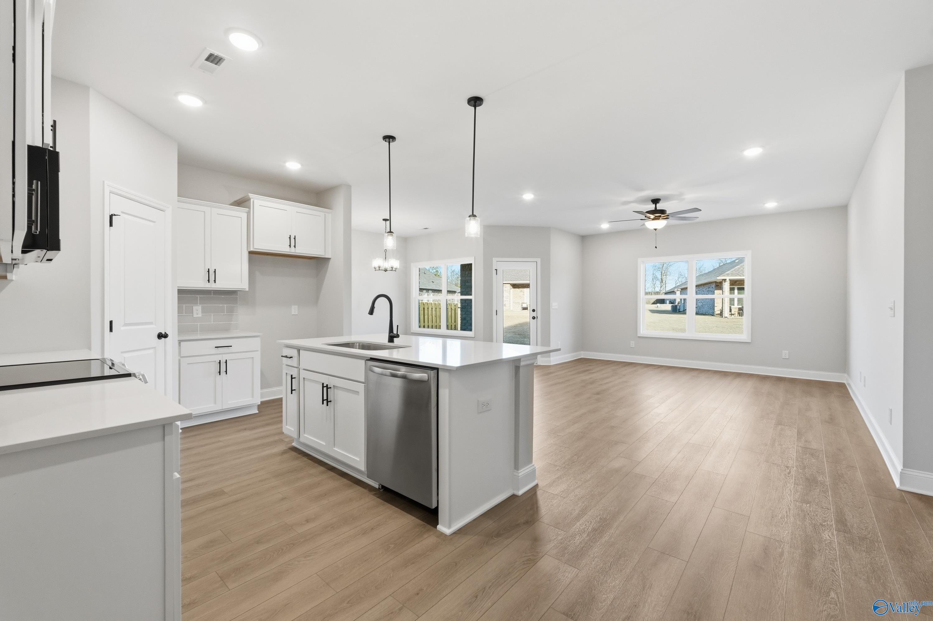 Modern open-concept kitchen with white cabinets, large island sink, and adjacent living area in The Daphne D 4-bedroom home, Arab, Alabama
