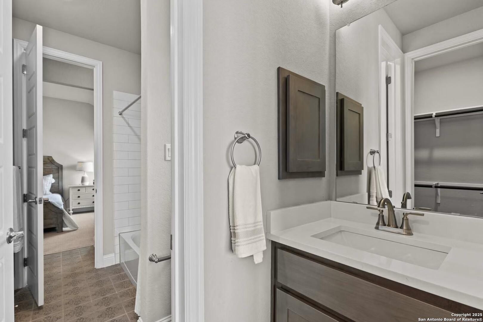 Modern master bathroom with white vanity, framed mirror, towel ring, and open door to adjoining bedroom in The Garner B, Castroville TX