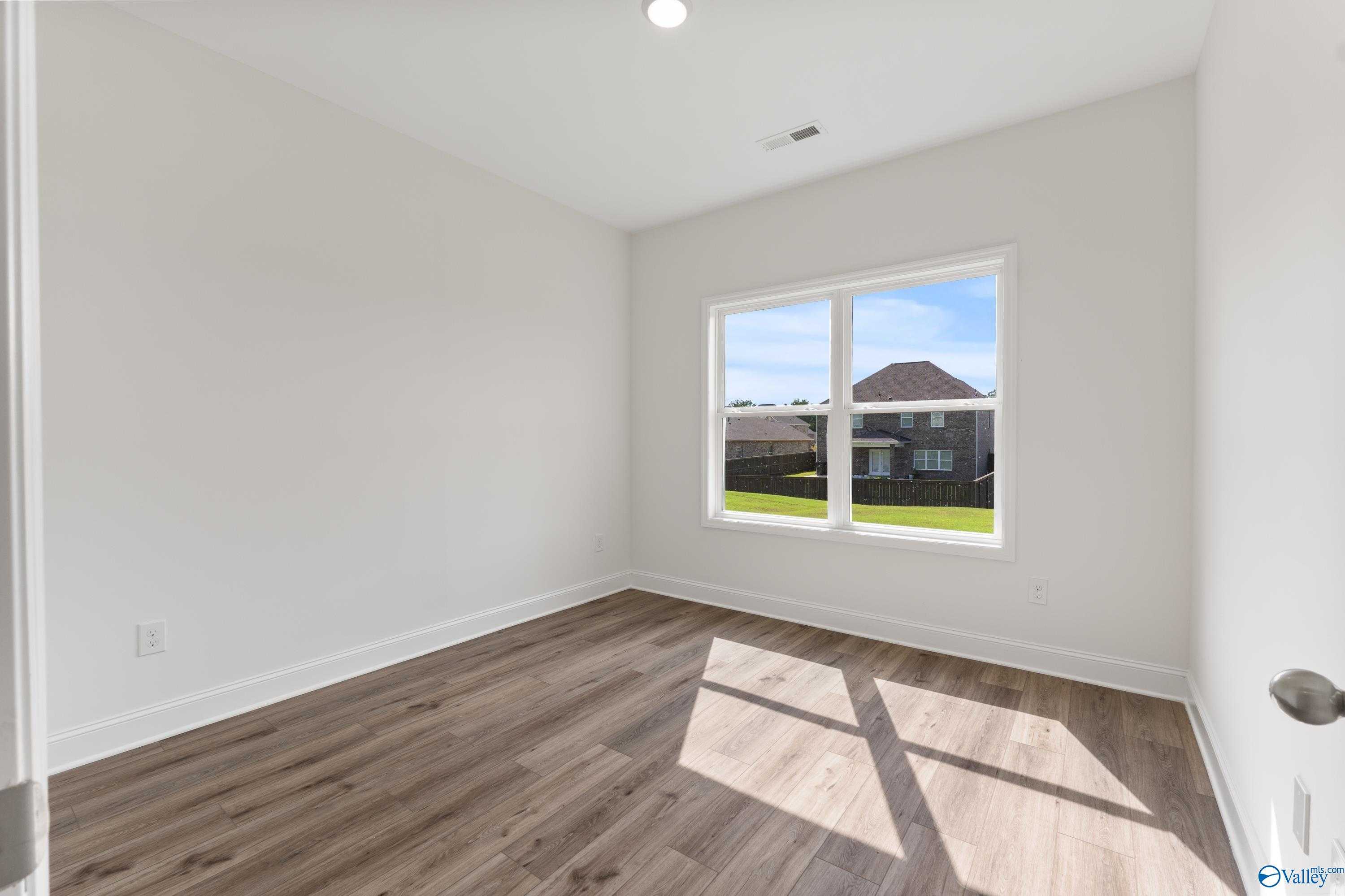 Bright secondary bedroom with light hardwood floors and large window view of green lawn in Davidson Homes The Shelby A, New Market, Alabama