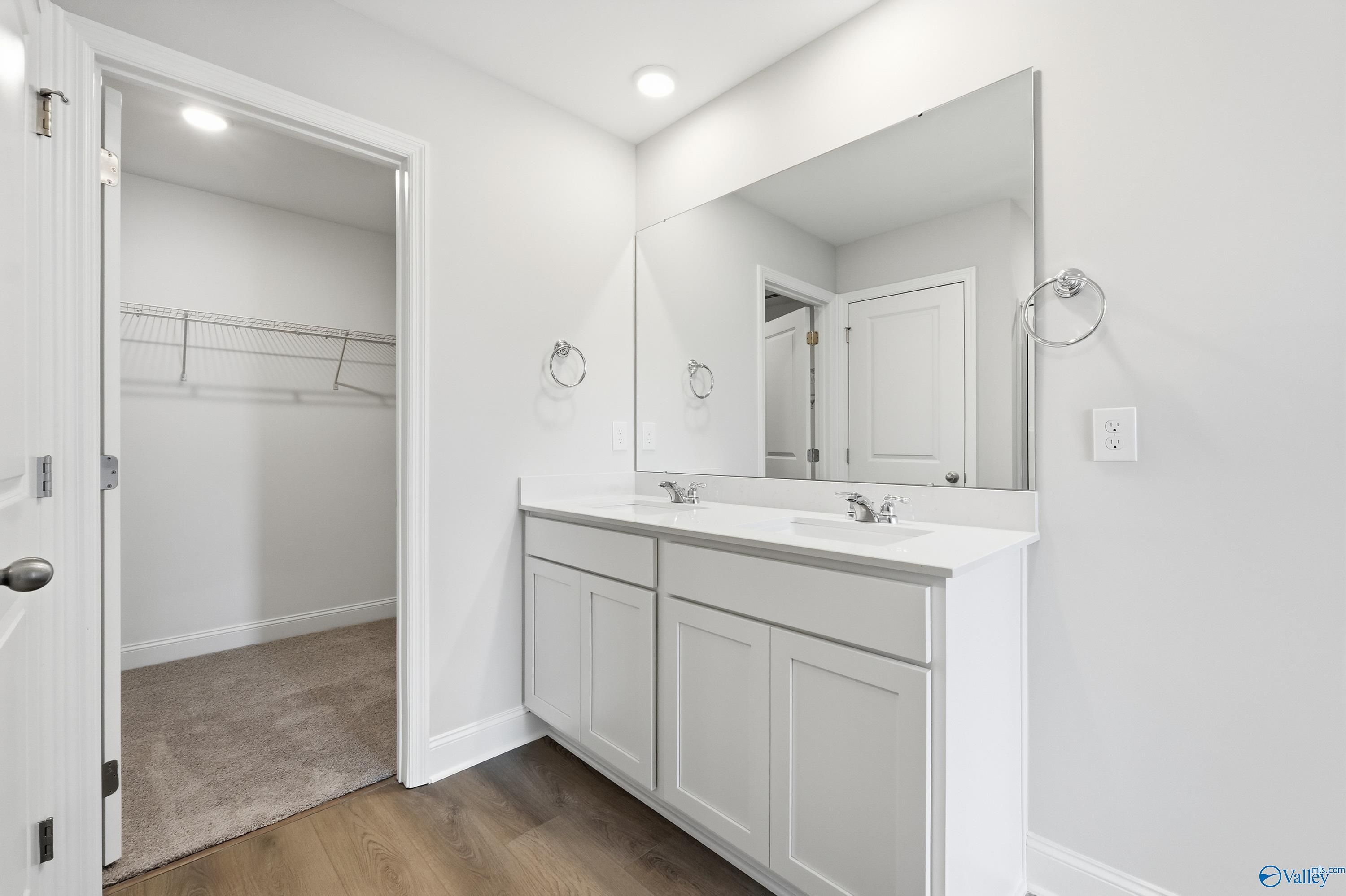 Modern master bathroom featuring double white vanity, large mirrors, and walk-in closet access in Davidson Homes The Franklin, New Market, Alabama