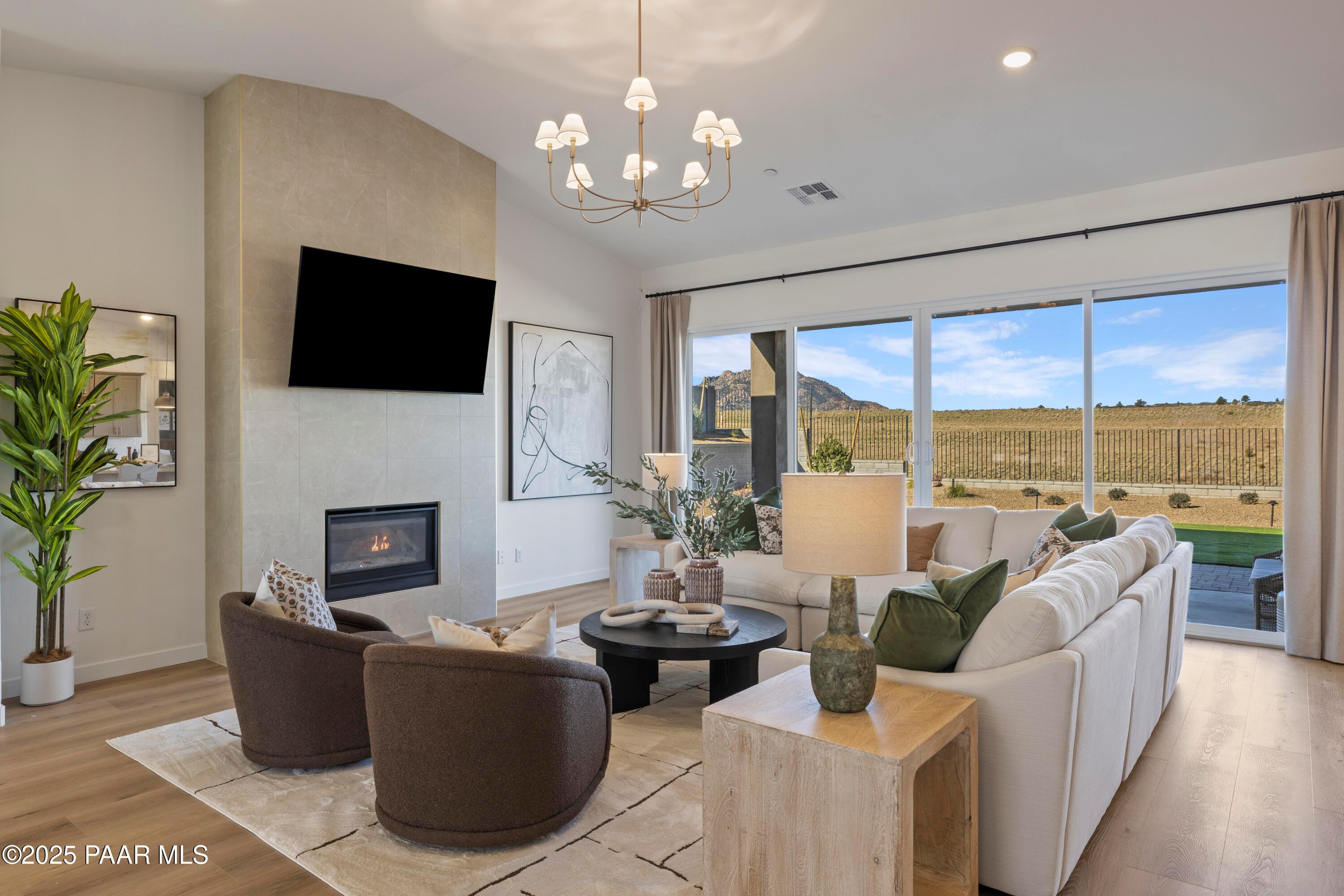 Cozy living room with stone gas fireplace, mounted TV, chandelier, and desert views via sliding glass doors in Davidson Homes The Blaze D, Prescott, Arizona