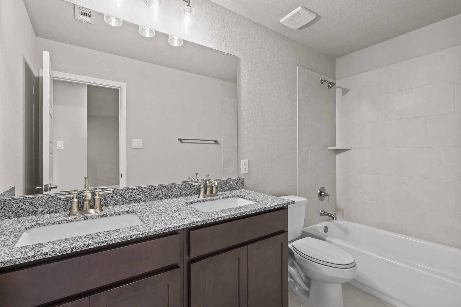 Spacious bathroom in The Jennings featuring a dual-sink granite vanity, dark wood cabinets, and a tiled shower-tub combo.