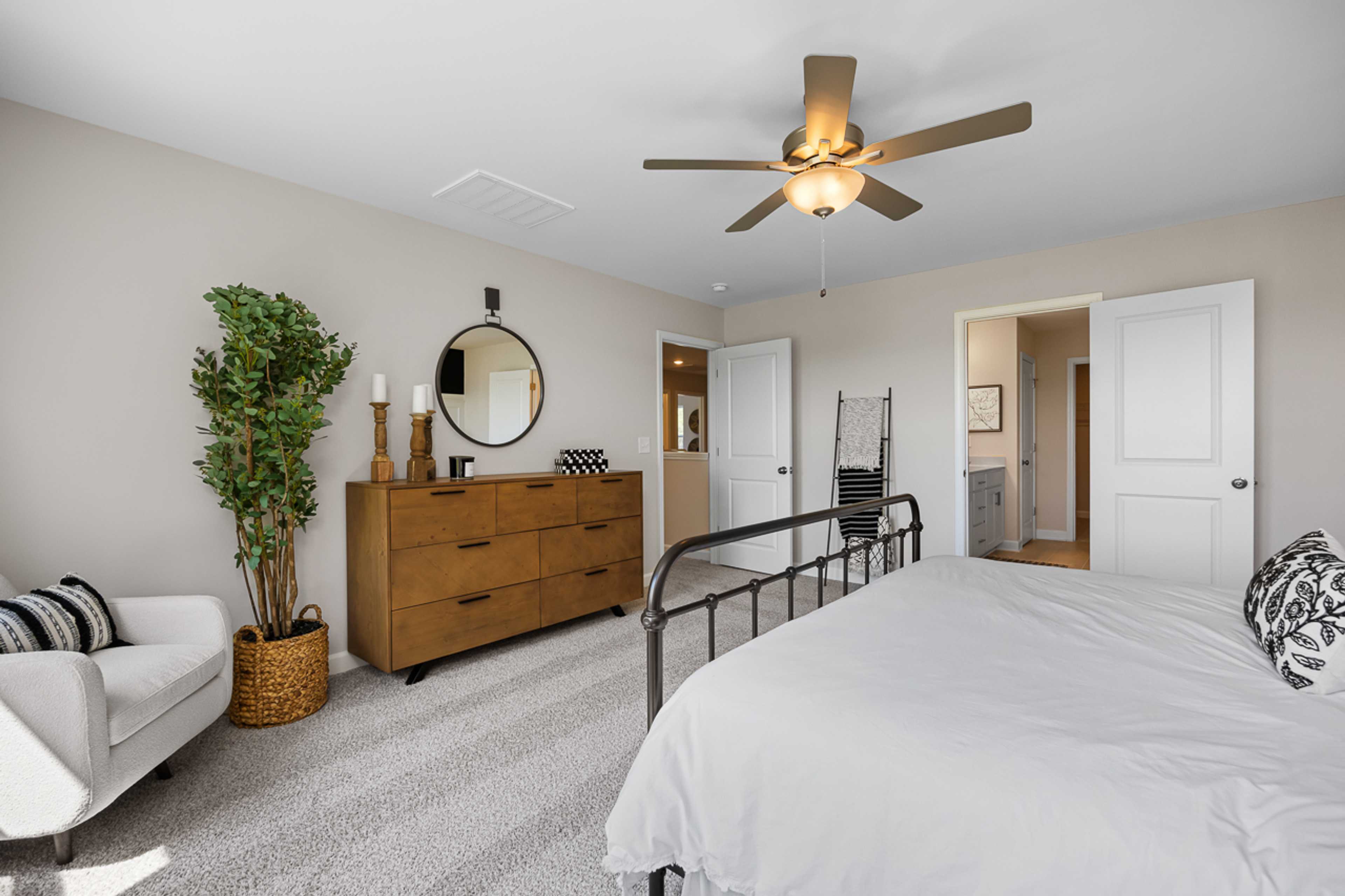 Spacious primary bedroom at Wellers Knoll in Lillington NC with king bed, wooden dresser, potted plant, and ceiling fan