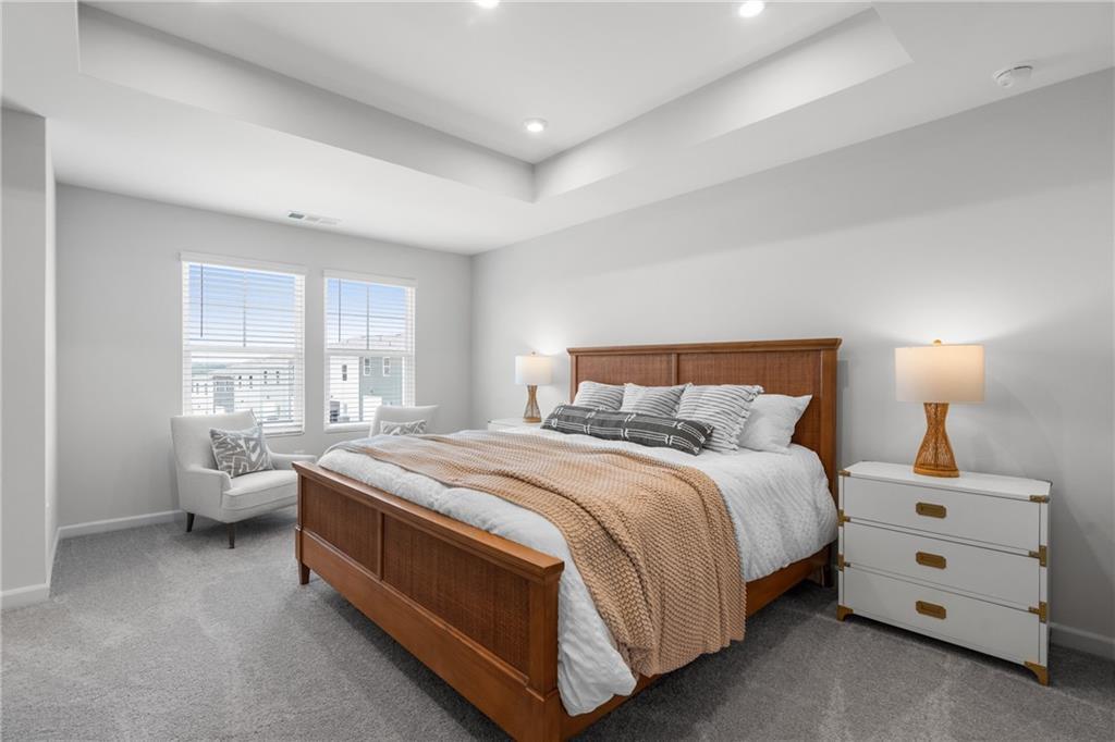 Serene master bedroom with wooden bed frame, plush neutral bedding, accent chair, and tray ceiling in Davidson Homes The Durant A, Emerson, GA