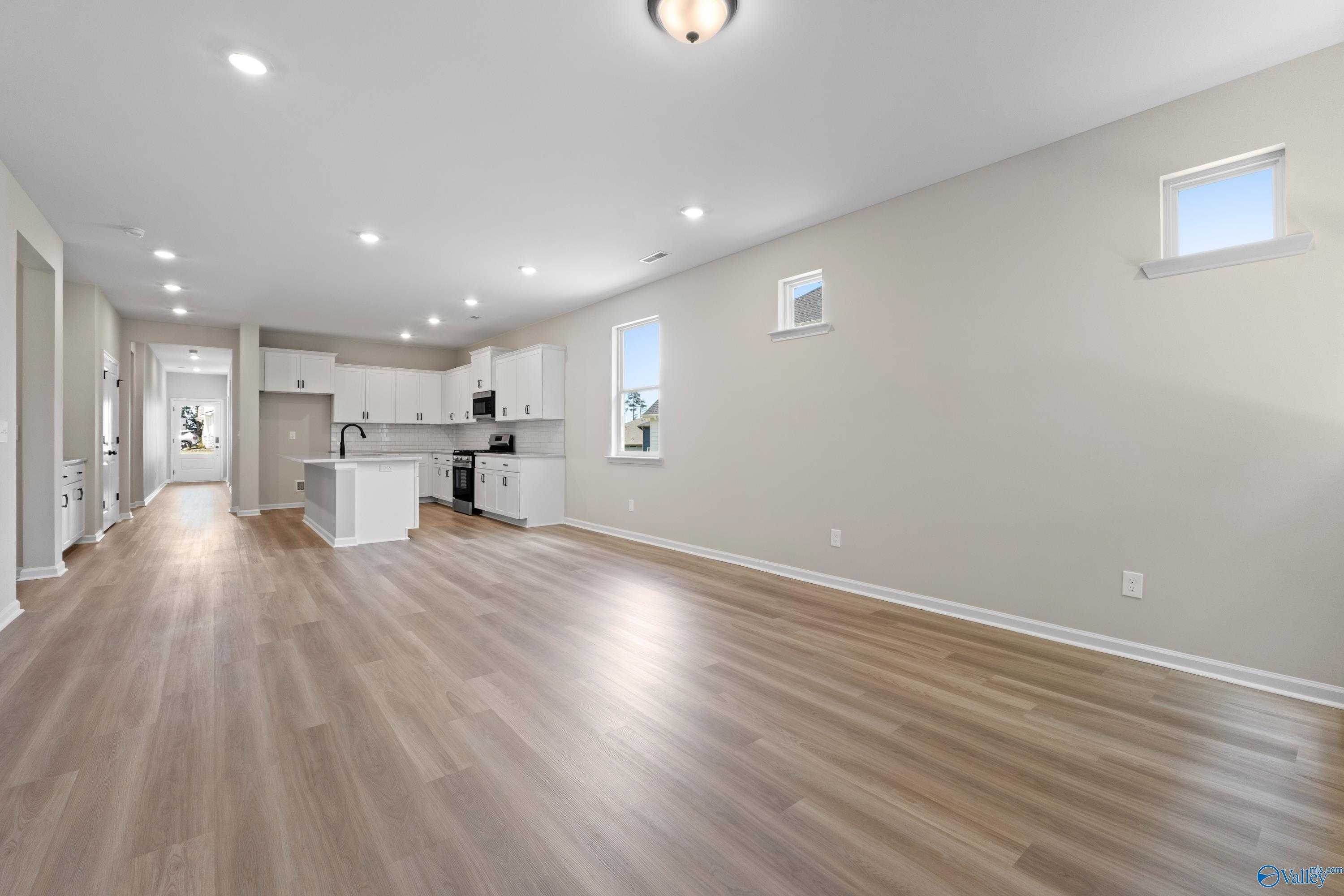 Open-concept kitchen with white shaker cabinets, large island, stainless appliances, and light wood laminate floors in The Nantucket by Evermore Homes, Madison, AL