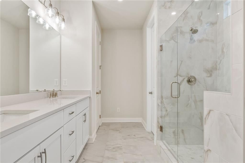 Modern master bathroom with white double vanity, frameless glass shower, and marble tiles in Davidson Homes The Danbury E, Buford, GA
