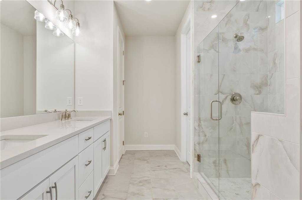 Modern master bathroom with white double vanity, frameless glass shower, and marble tiles in Davidson Homes The Danbury E, Buford, GA