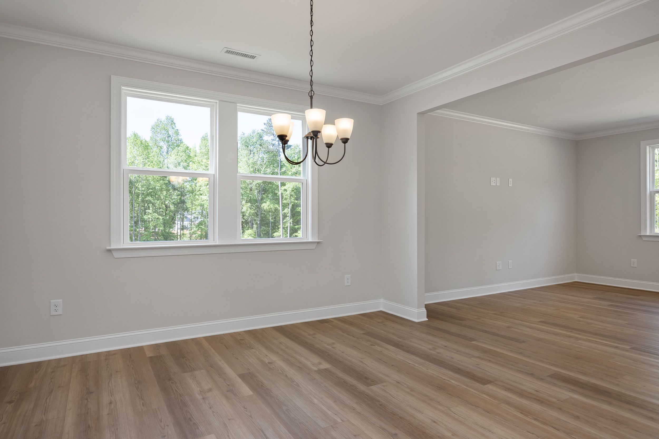 Bright dining room in The Beech A featuring hardwood floors, four-light chandelier, and large windows with tree views