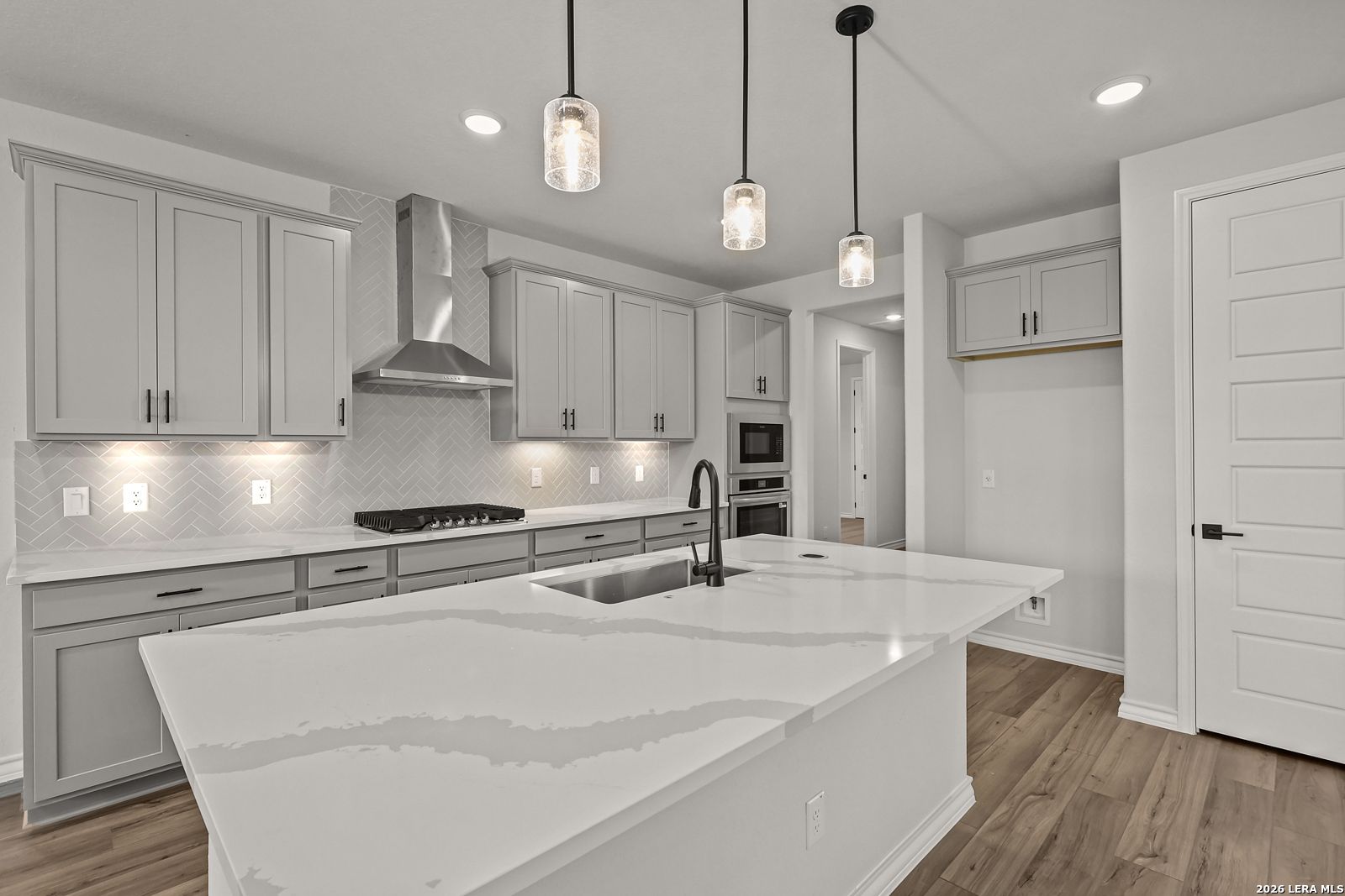 Modern kitchen with gray cabinetry, quartz island, and pendant lights in The Oxford F floor plan at Potranco Oaks, Castroville, TX