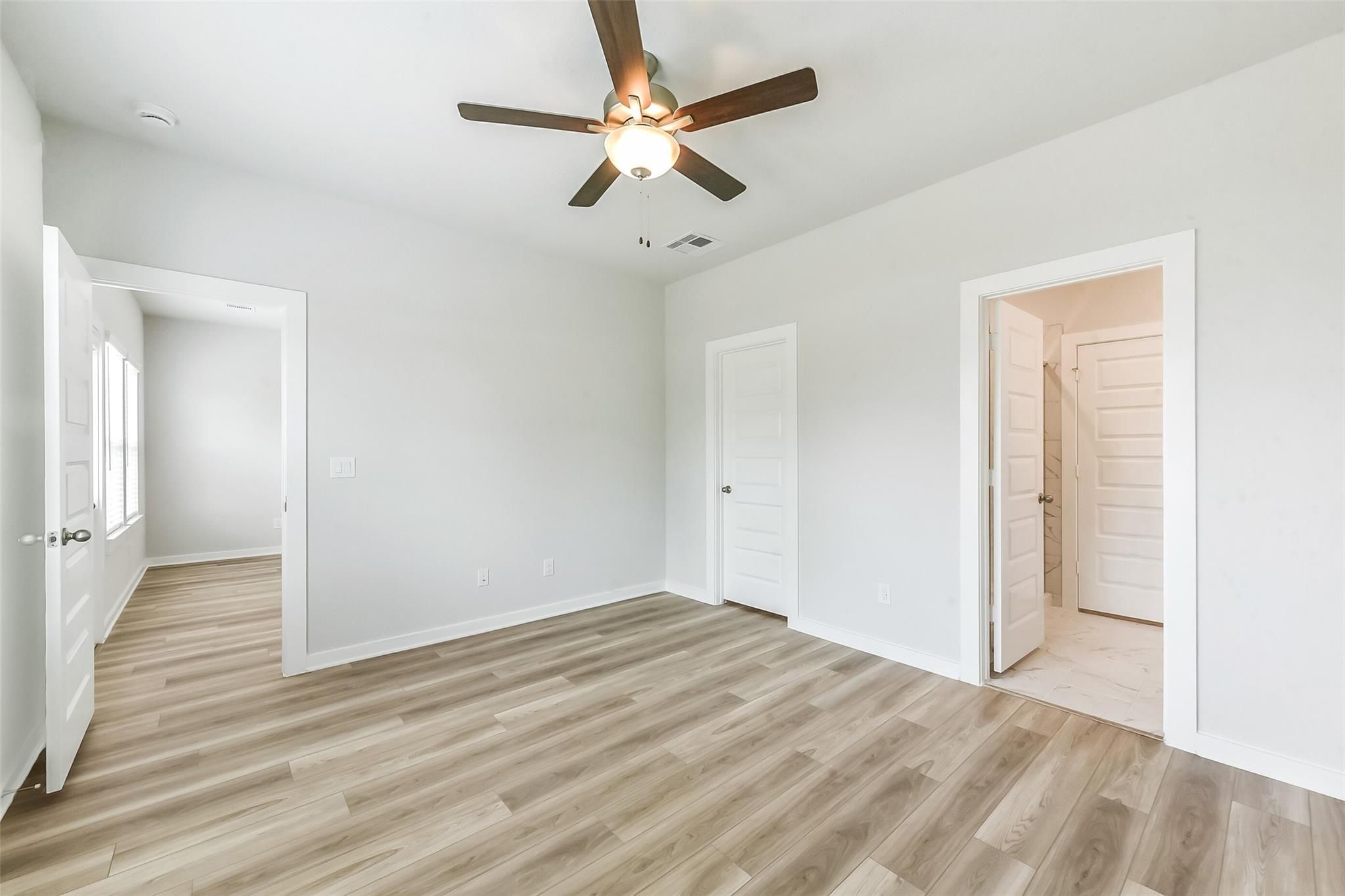 Spacious secondary bedroom with ceiling fan, laminate wood floors, and en-suite bathroom in Davidson Homes The Frio G, Magnolia Texas