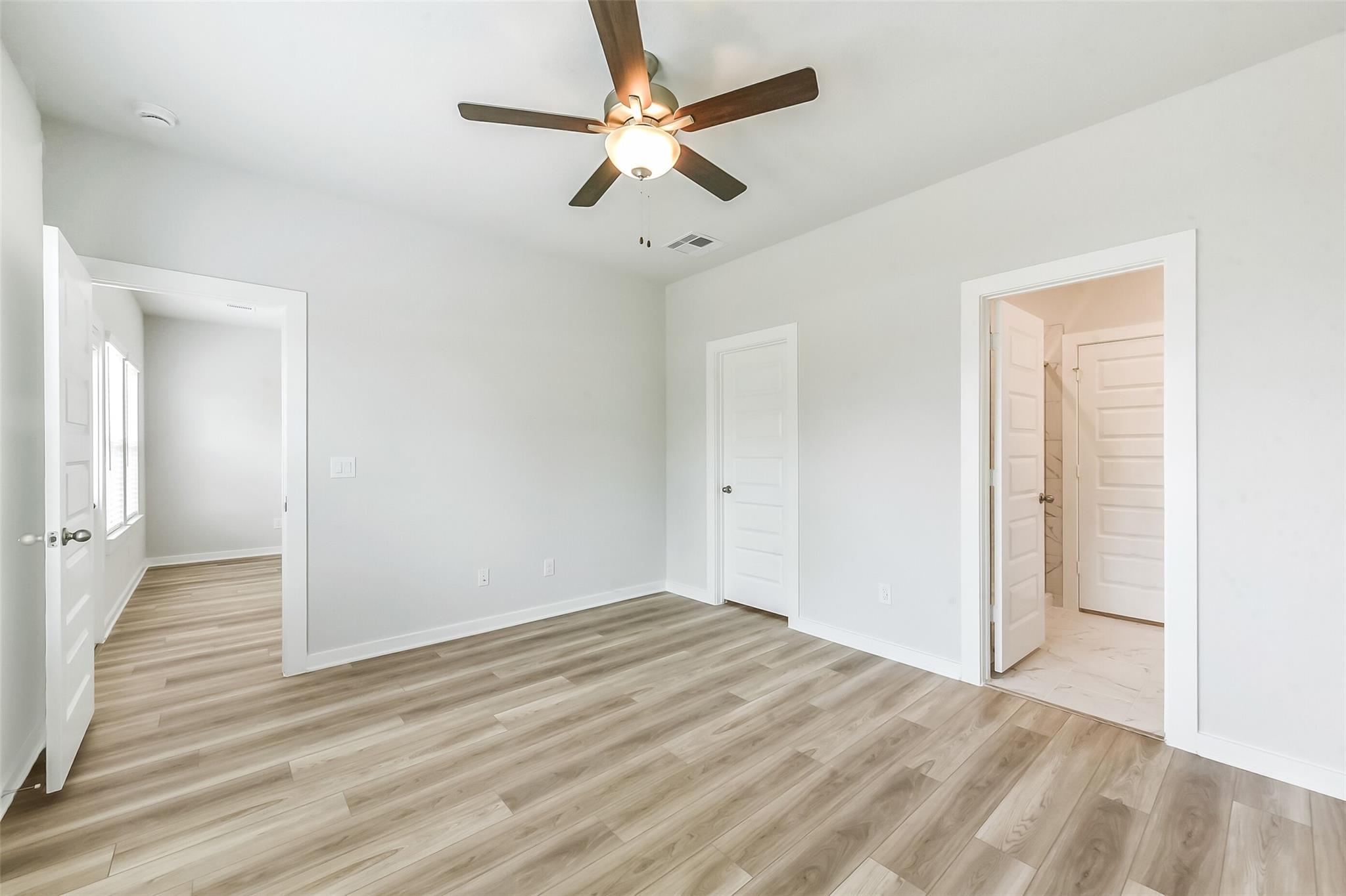 Spacious secondary bedroom with ceiling fan, laminate wood floors, and en-suite bathroom in Davidson Homes The Frio G, Magnolia Texas
