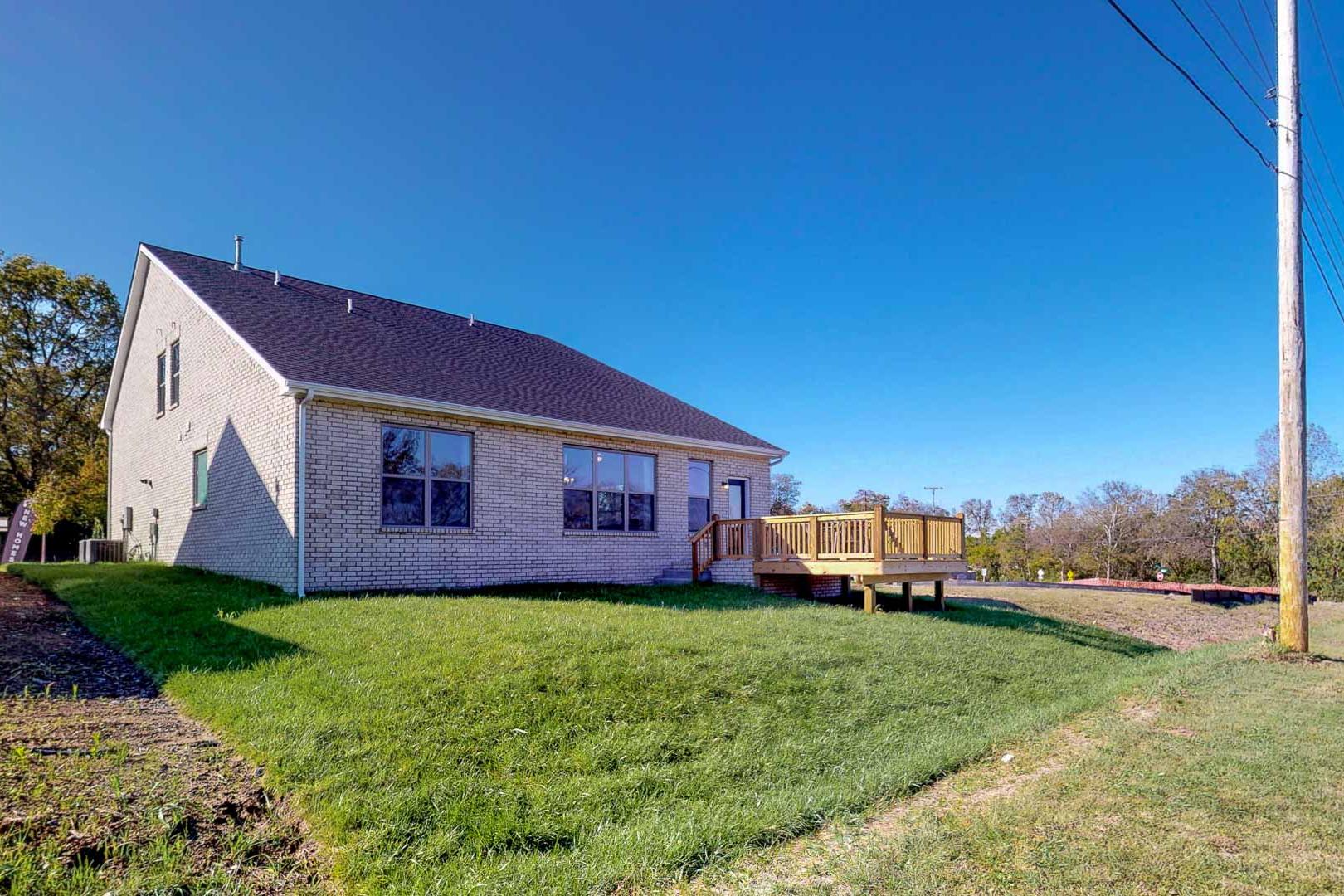 Side view of modern brick home at Liberty Creek in Gallatin TN with wooden deck, green lawn, and autumn trees
