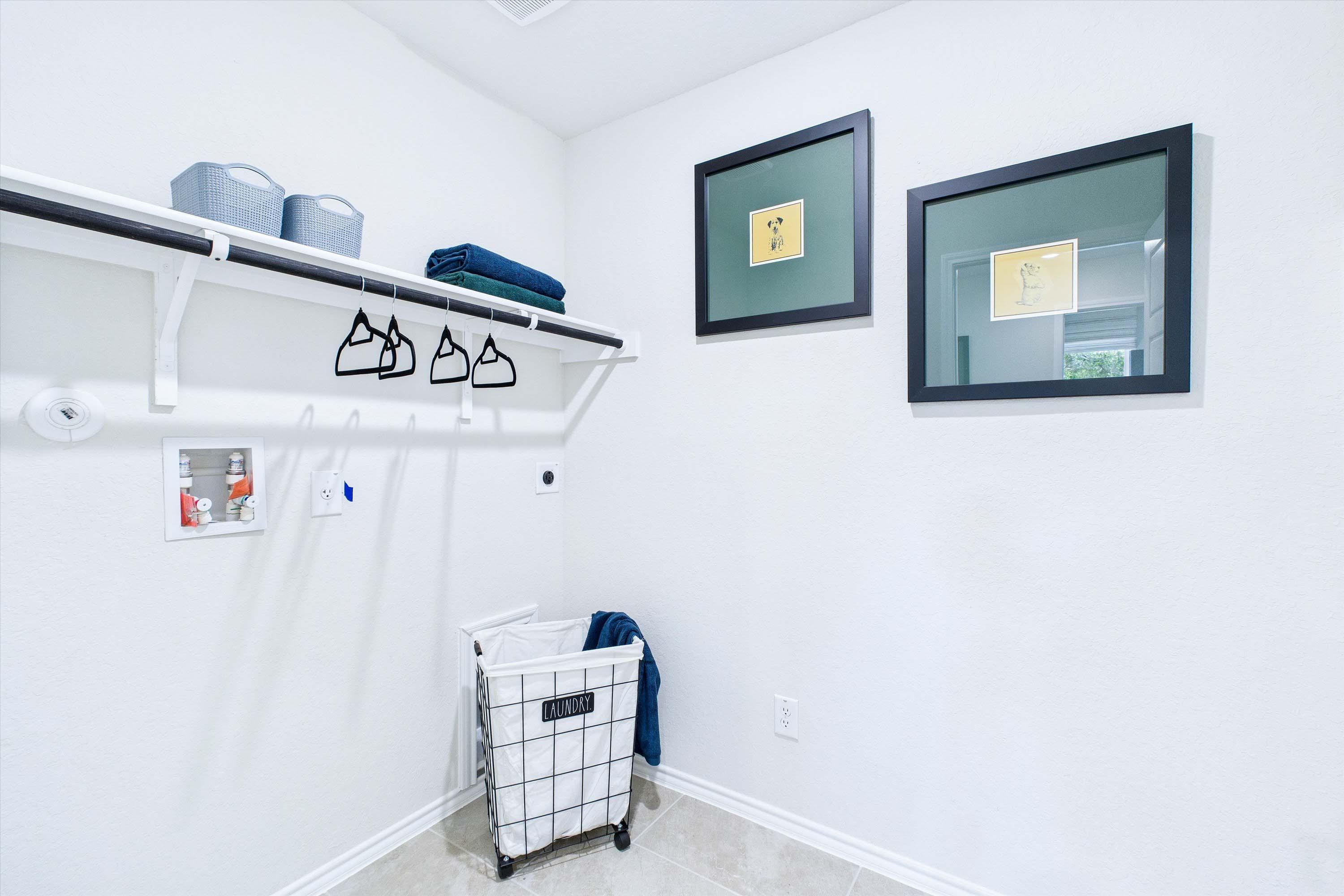 Bright laundry room in The Gillian C by Davidson Homes, featuring shelving, a rolling laundry basket, and decor.