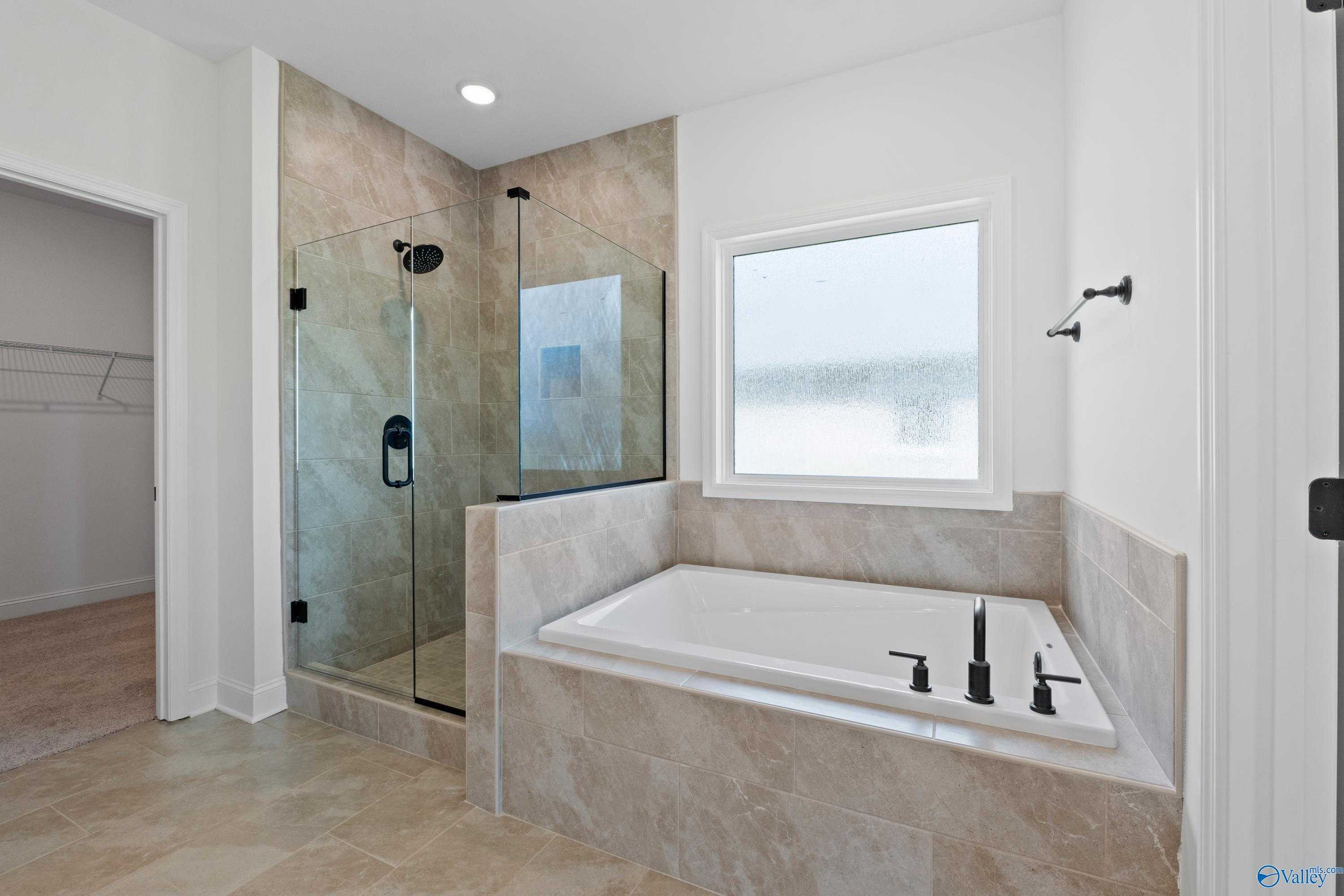 Luxurious master bathroom with glass-enclosed shower, soaking tub, and walk-in closet in Davidson Homes The Rockford B, Toney, Alabama