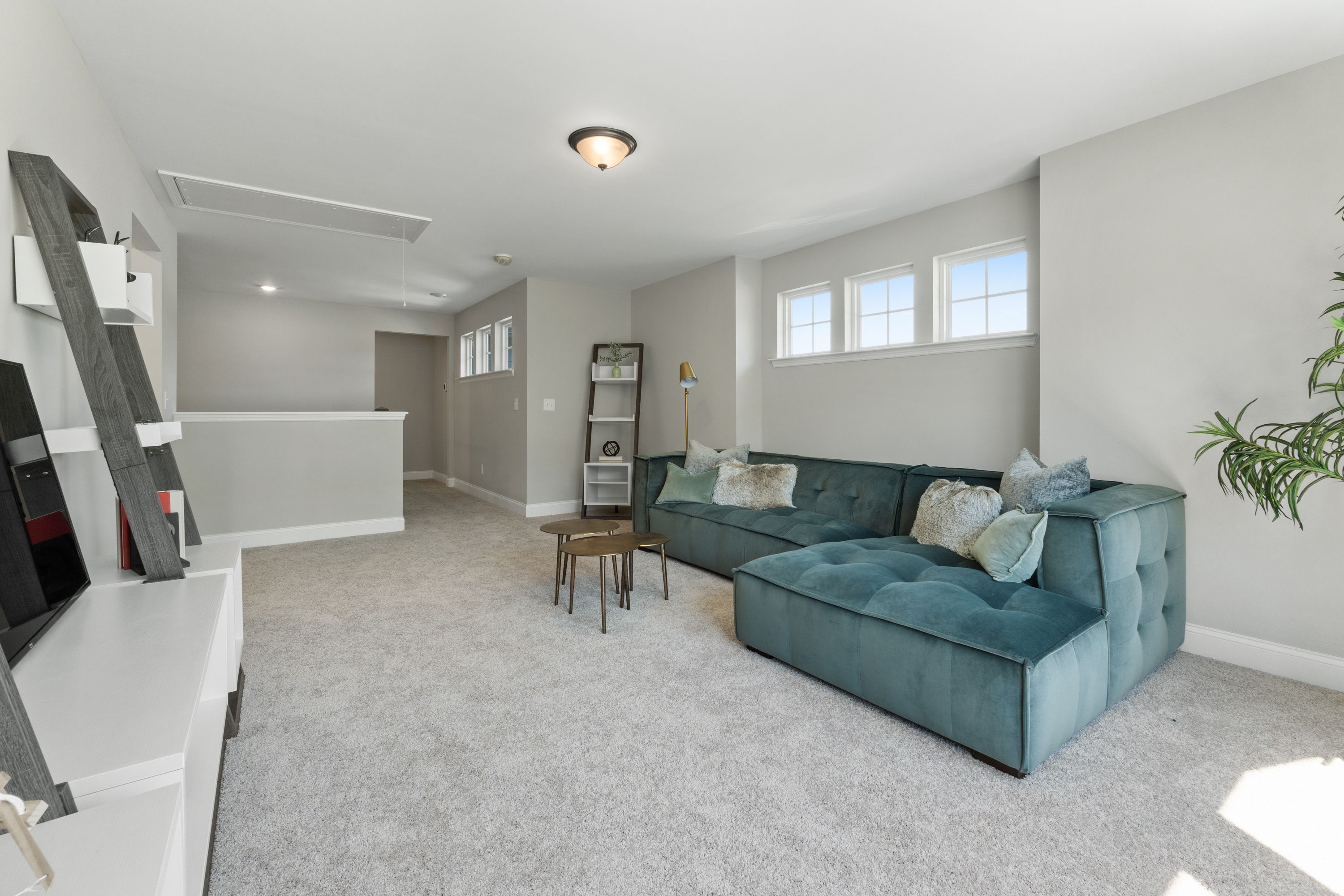 Spacious bonus room in The Haven D with teal velvet L-shaped sofa, media console, shelves and natural light