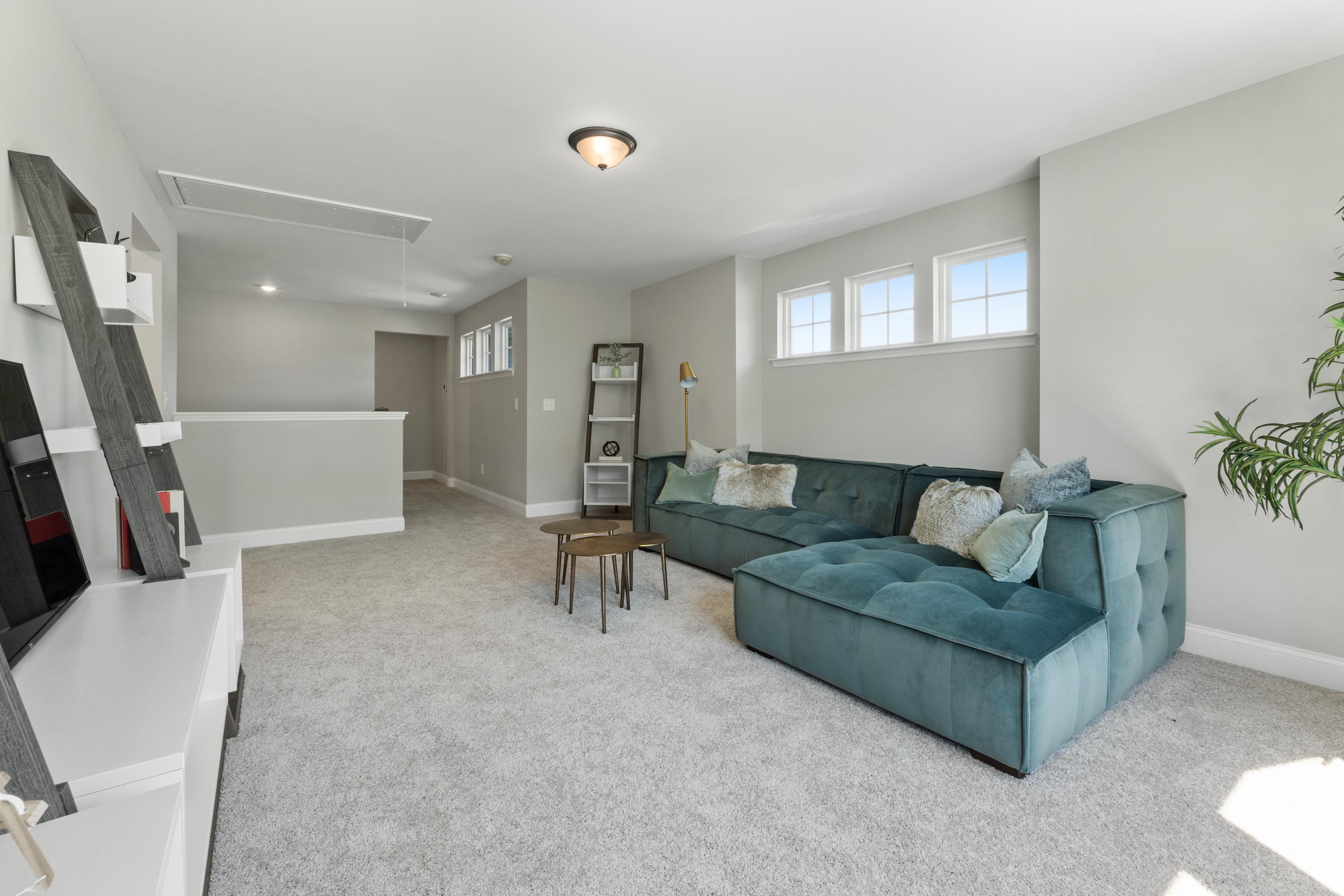Spacious bonus room in The Haven D with teal velvet L-shaped sofa, media console, shelves and natural light