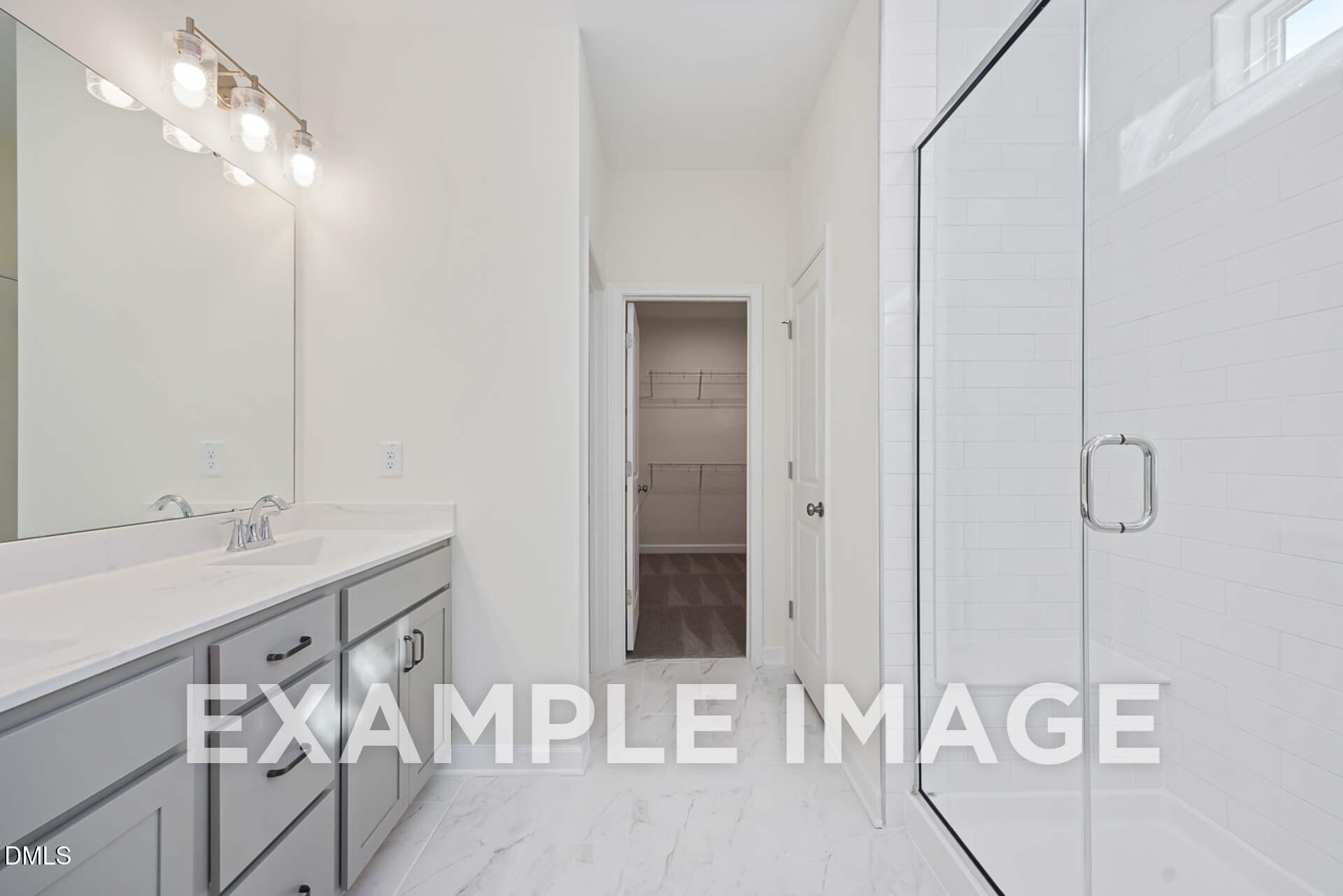 Modern master bathroom with quartz vanity, large mirror, frameless glass shower, and walk-in closet in Davidson Homes The Ash B, Zebulon NC