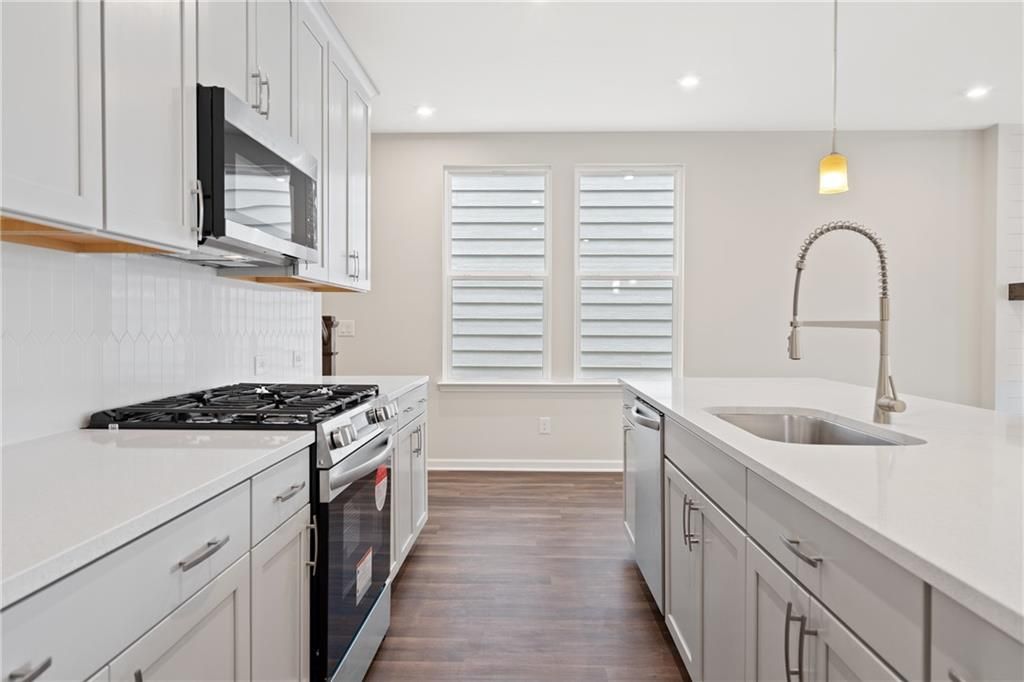 Modern white kitchen with shaker cabinets, stainless steel appliances, quartz island, and gooseneck faucet in Davidson Homes The Cary B, Kennesaw, GA