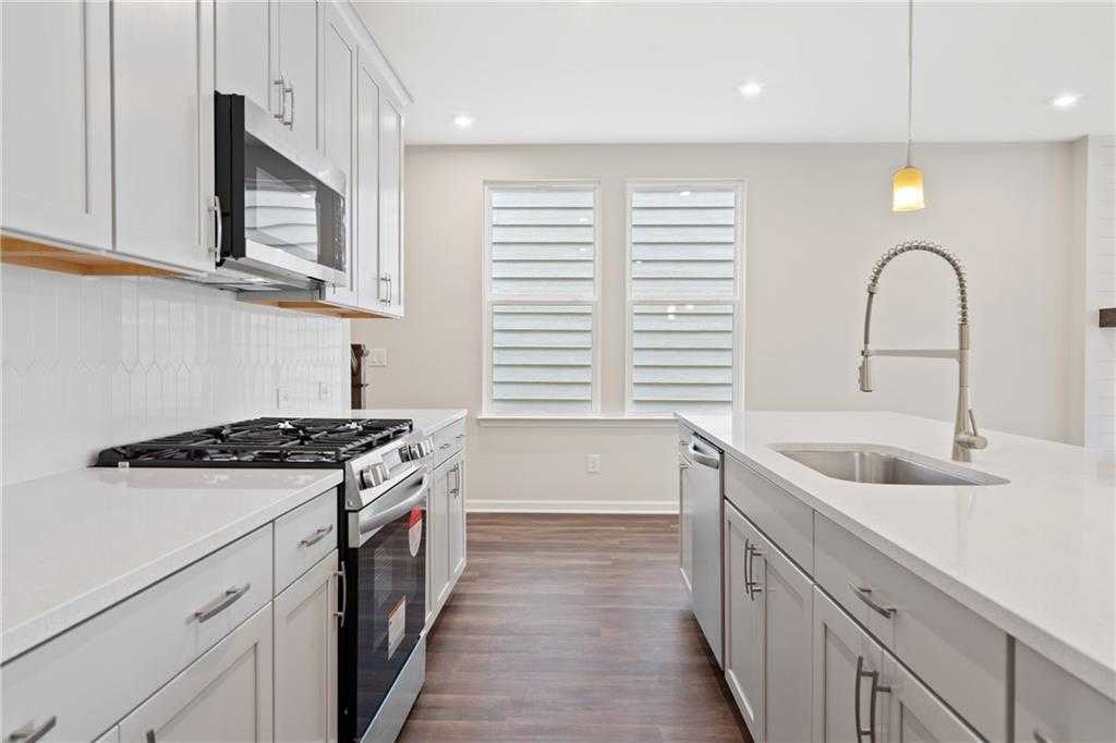 Modern white kitchen with shaker cabinets, stainless steel appliances, quartz island, and gooseneck faucet in Davidson Homes The Cary B, Kennesaw, GA