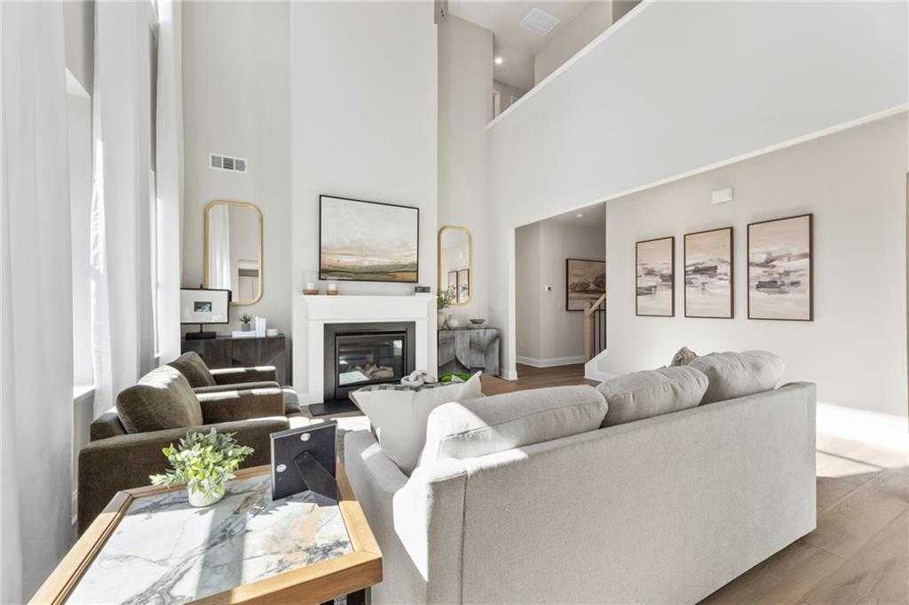 Cozy living room with gas fireplace, beige sofa, gold mirror, abstract art, and balcony in Davidson Homes The Danbury C, Buford, GA