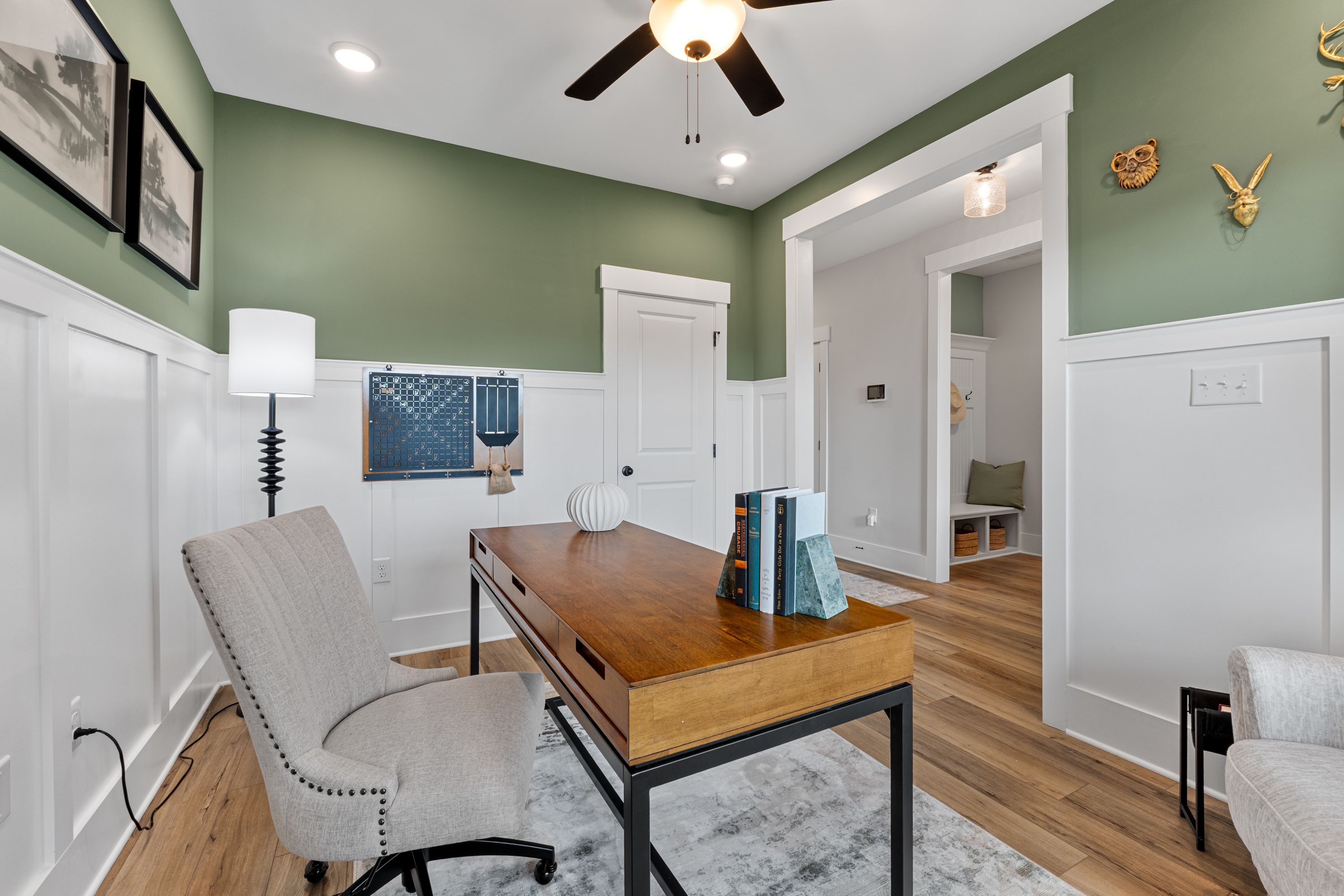 Cozy sage green home office at River Road Estates in Decatur AL with wooden desk, upholstered chair, and ceiling fan