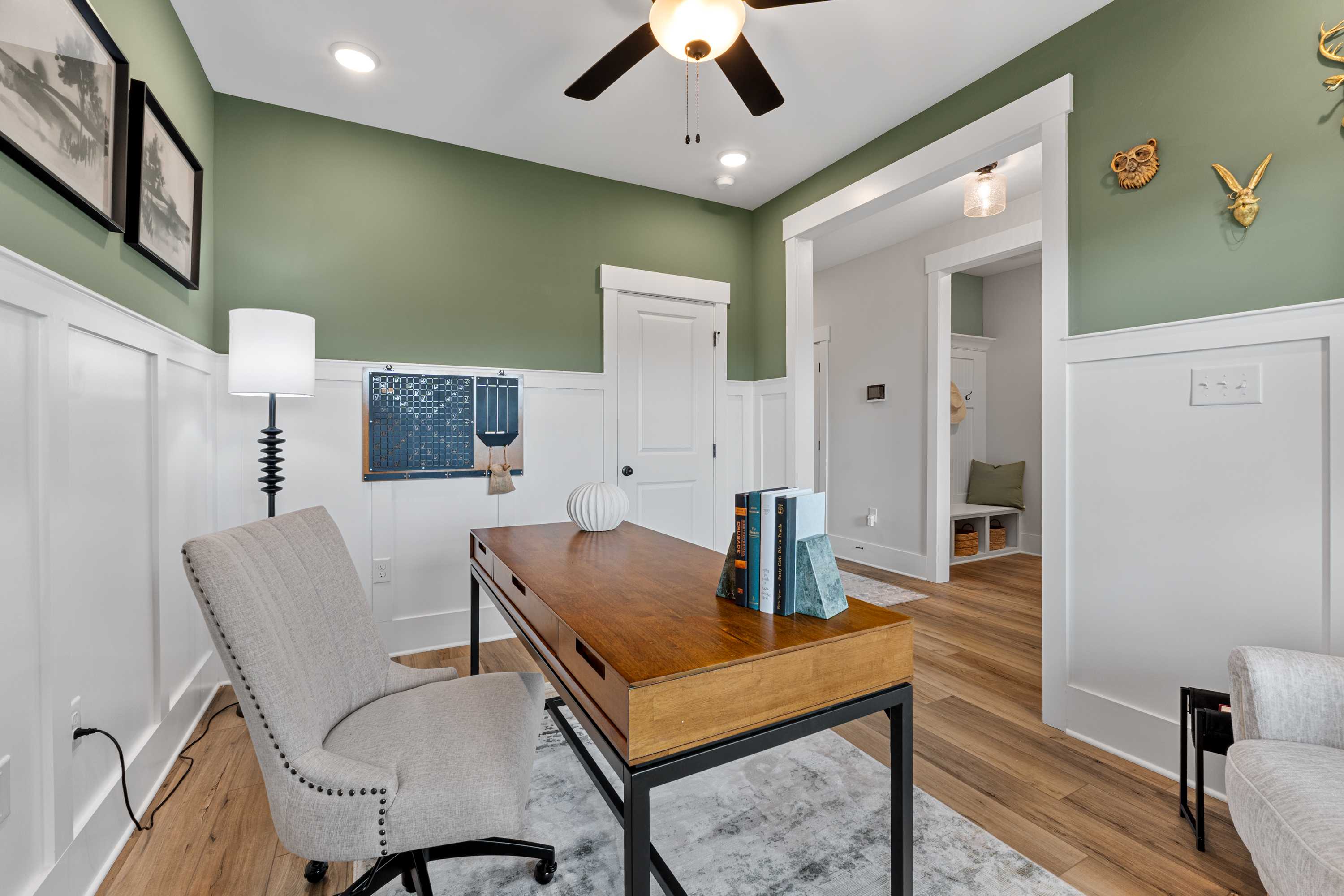 Cozy sage green home office at River Road Estates in Decatur AL with wooden desk, upholstered chair, and ceiling fan